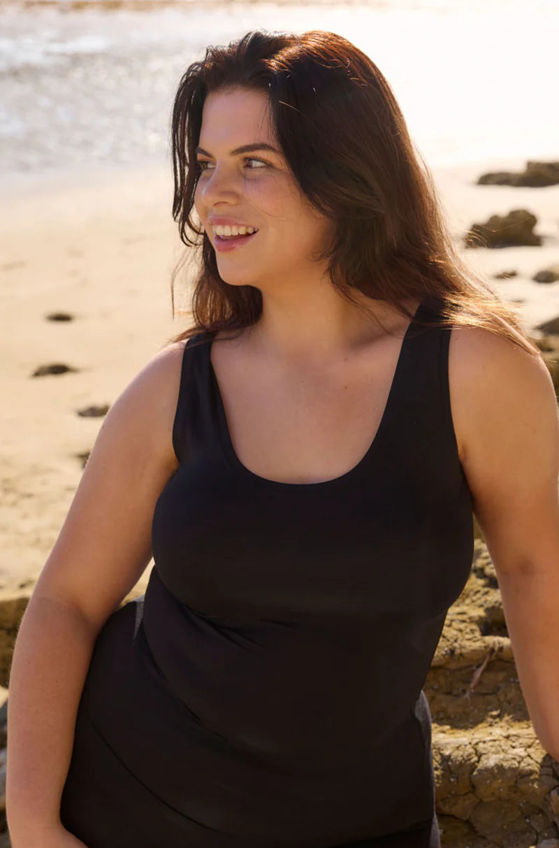 Woman wearing a black scoop neck tank top at the beach with ocean and rocks in the background