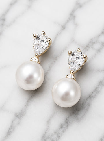 Pearl drop earrings with heart-shaped crystals on marble background