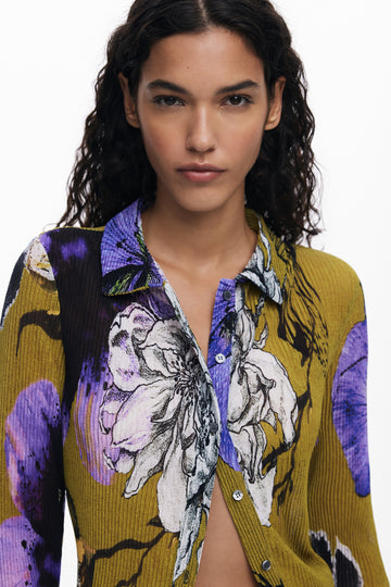 Woman wearing a mustard floral long sleeve shirt with purple and white print on a white background
