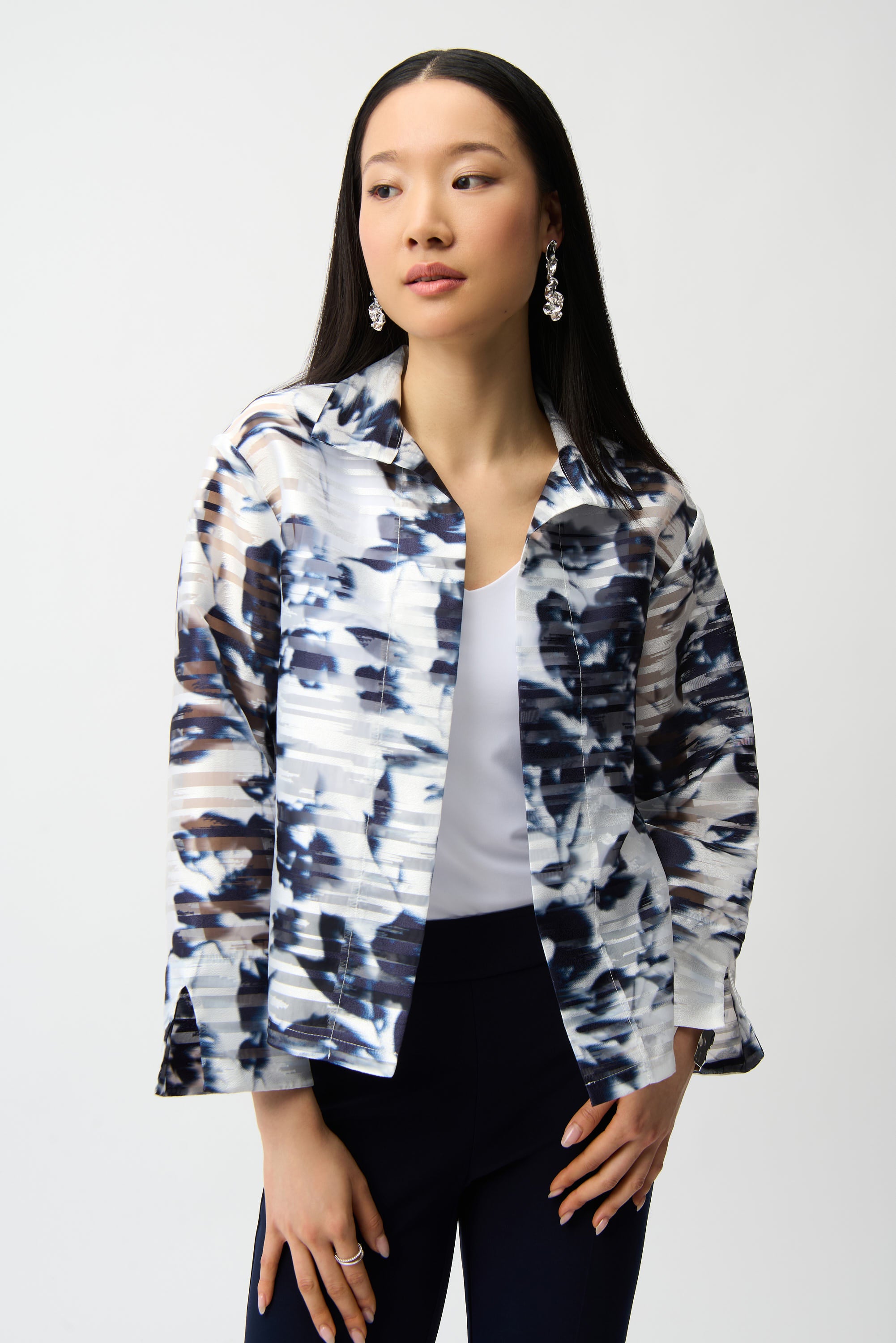 Woman wearing blue and white abstract print jacket with structured fit, layered over white top and dark pants, studio outfit look on white background