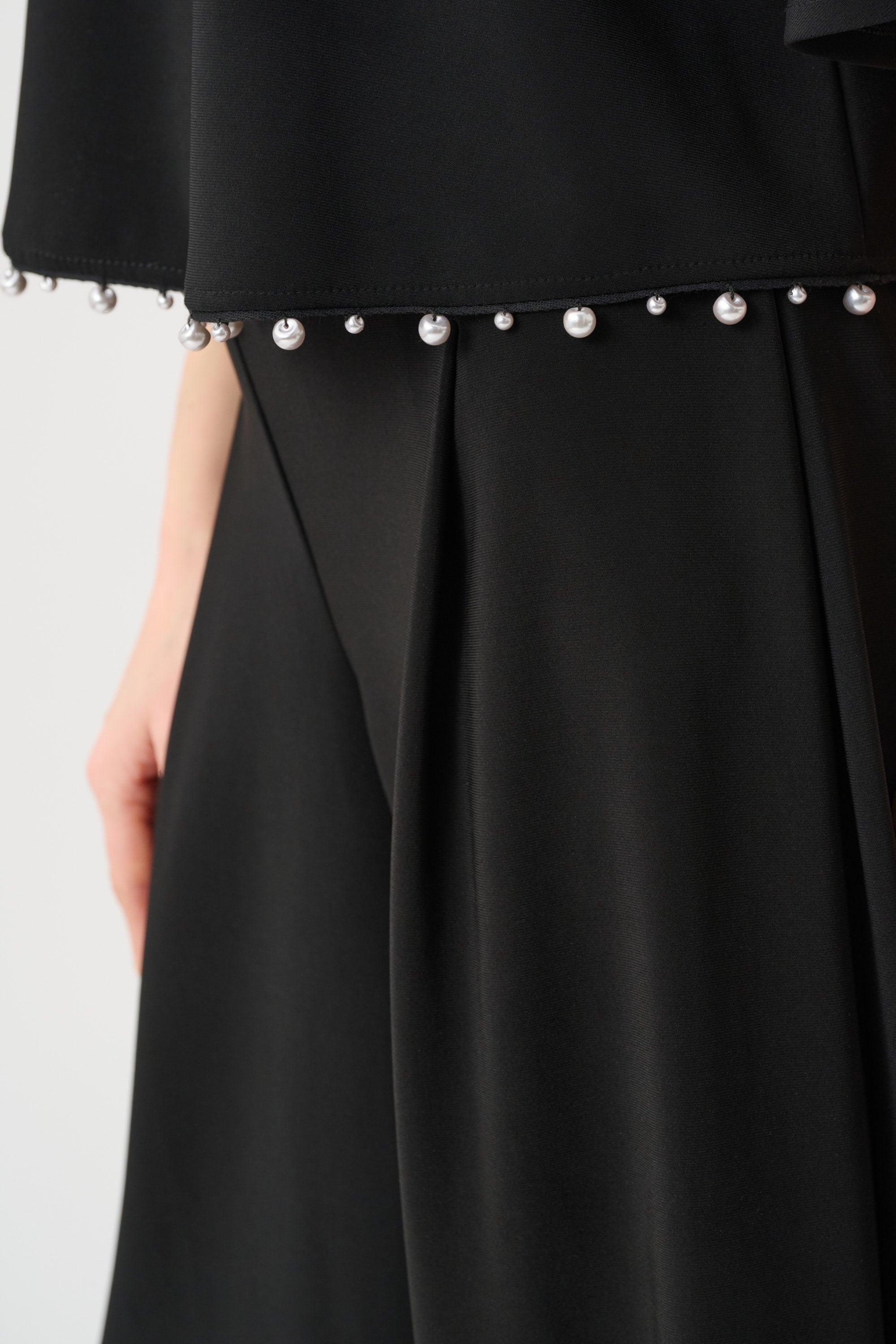 Close-up of black top with pearl trim hem and silky knit texture