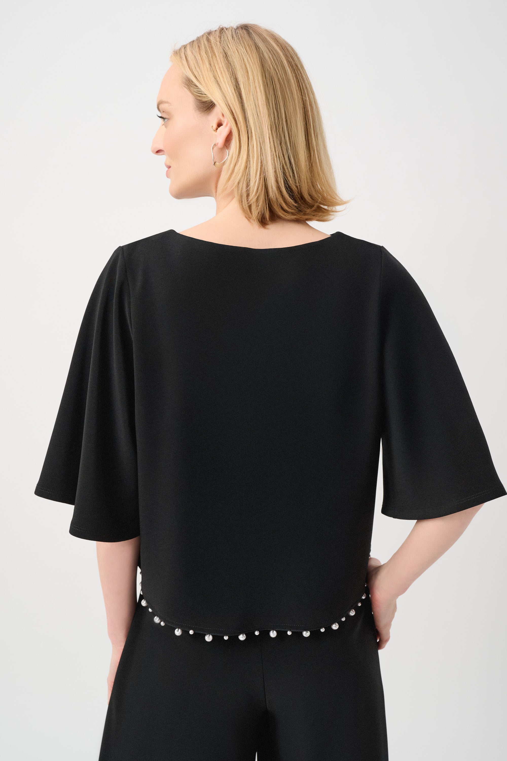 Back view of black flared sleeve top with pearl detail hem