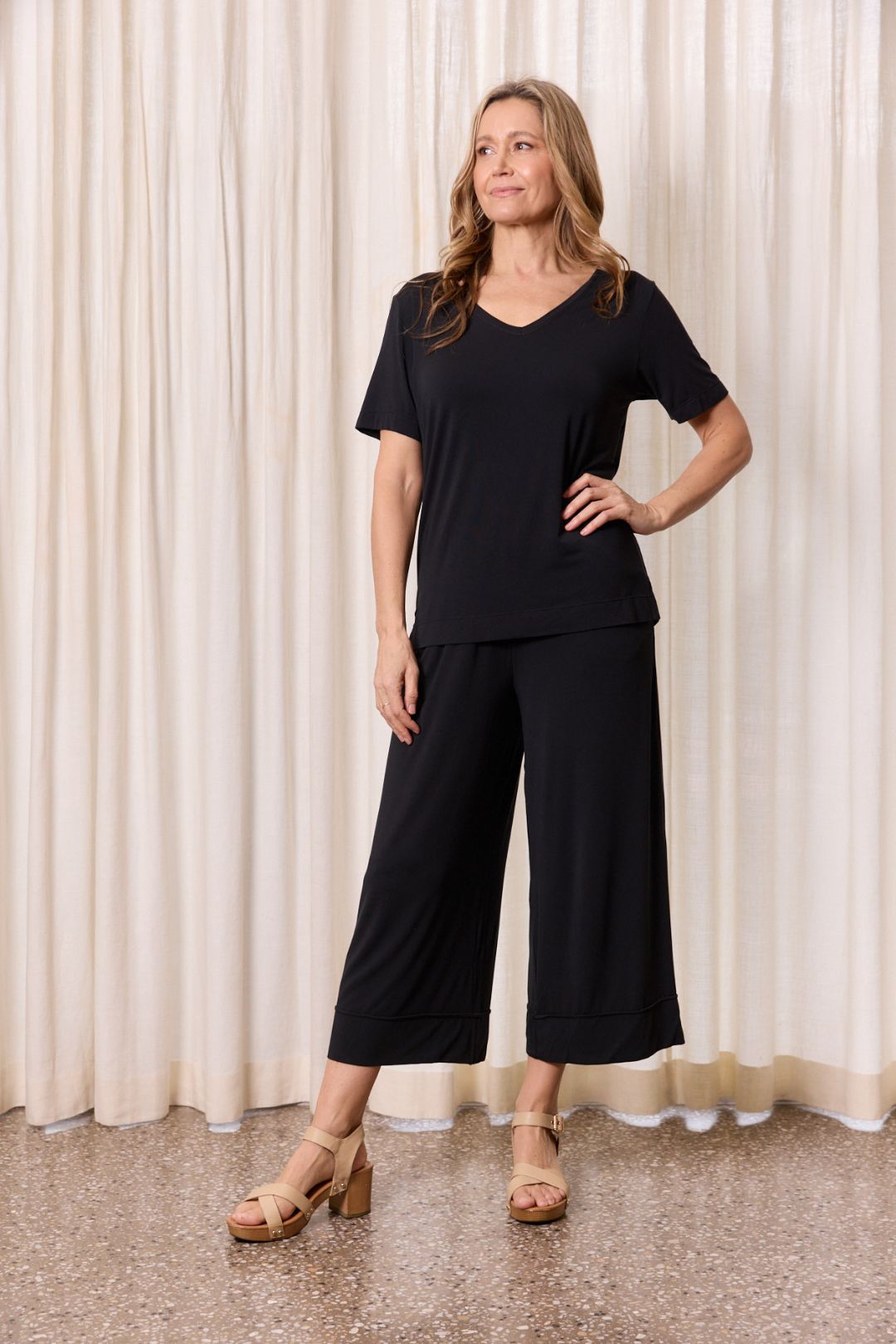 Woman wearing black casual outfit posing against neutral curtain indoor