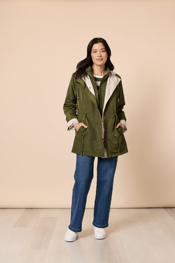 Woman in khaki green jacket with hood and blue jeans on beige background