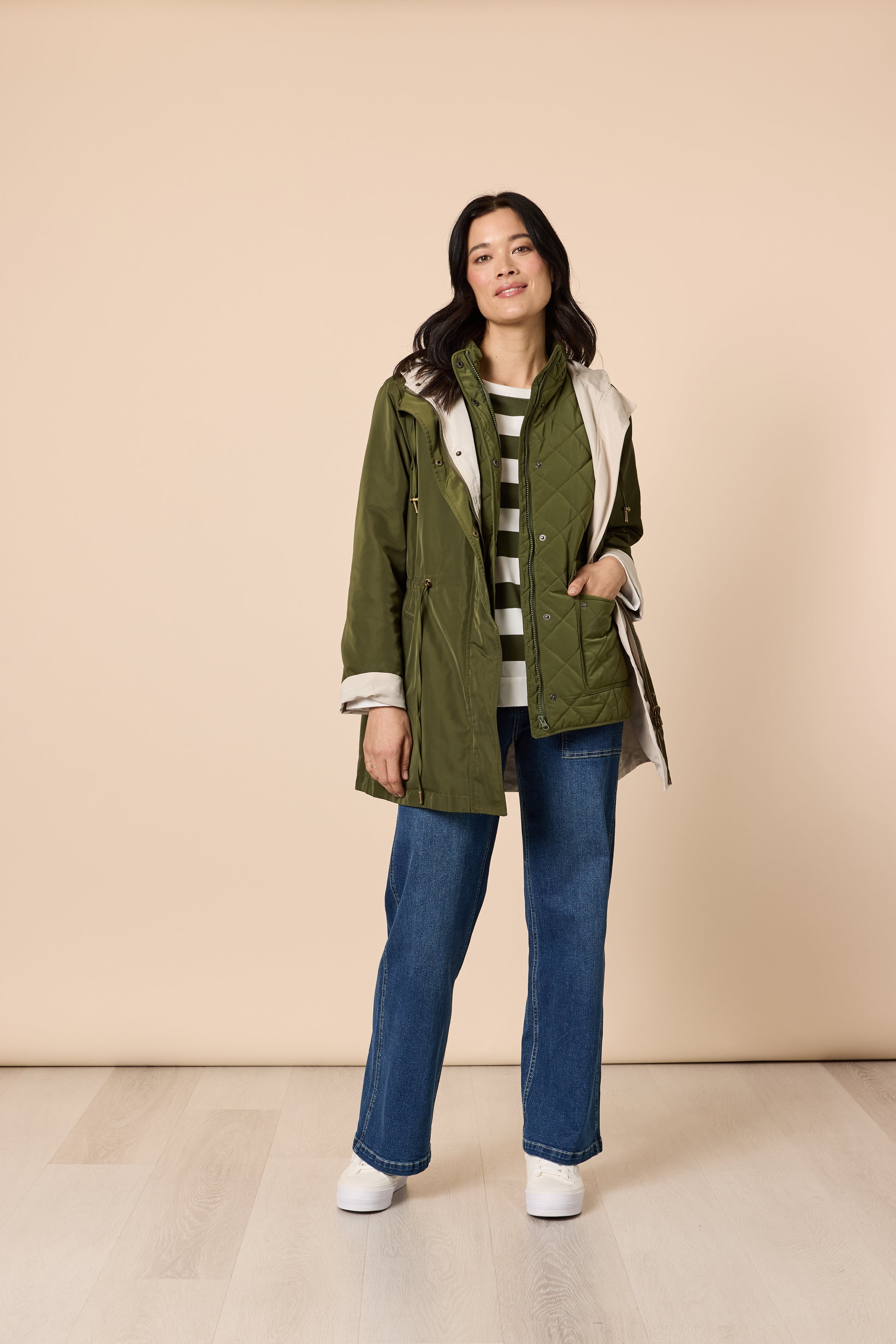 Front view of woman in khaki jacket layered with striped knit and denim jeans