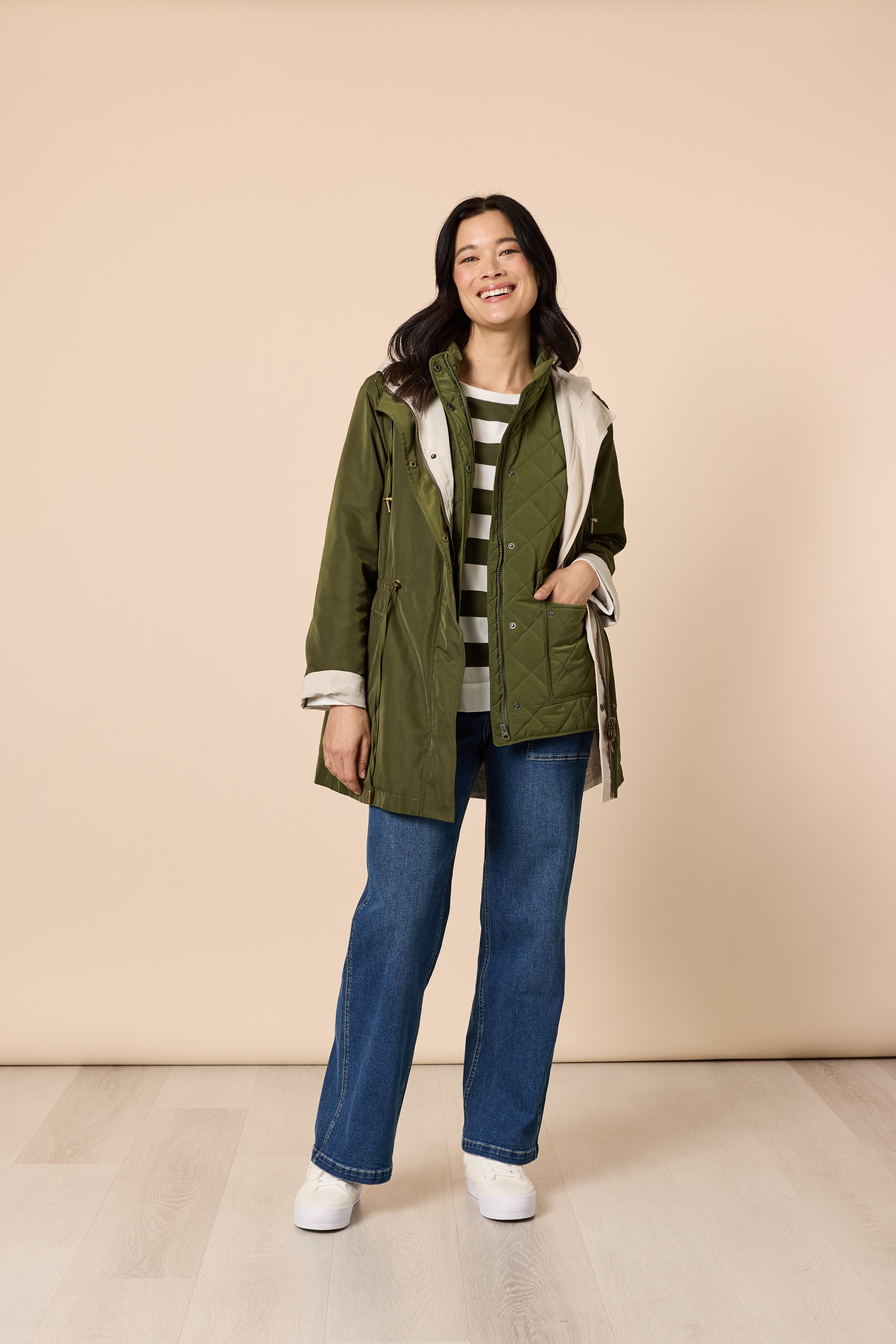 Smiling woman in casual green jacket outfit with striped top and blue jeans