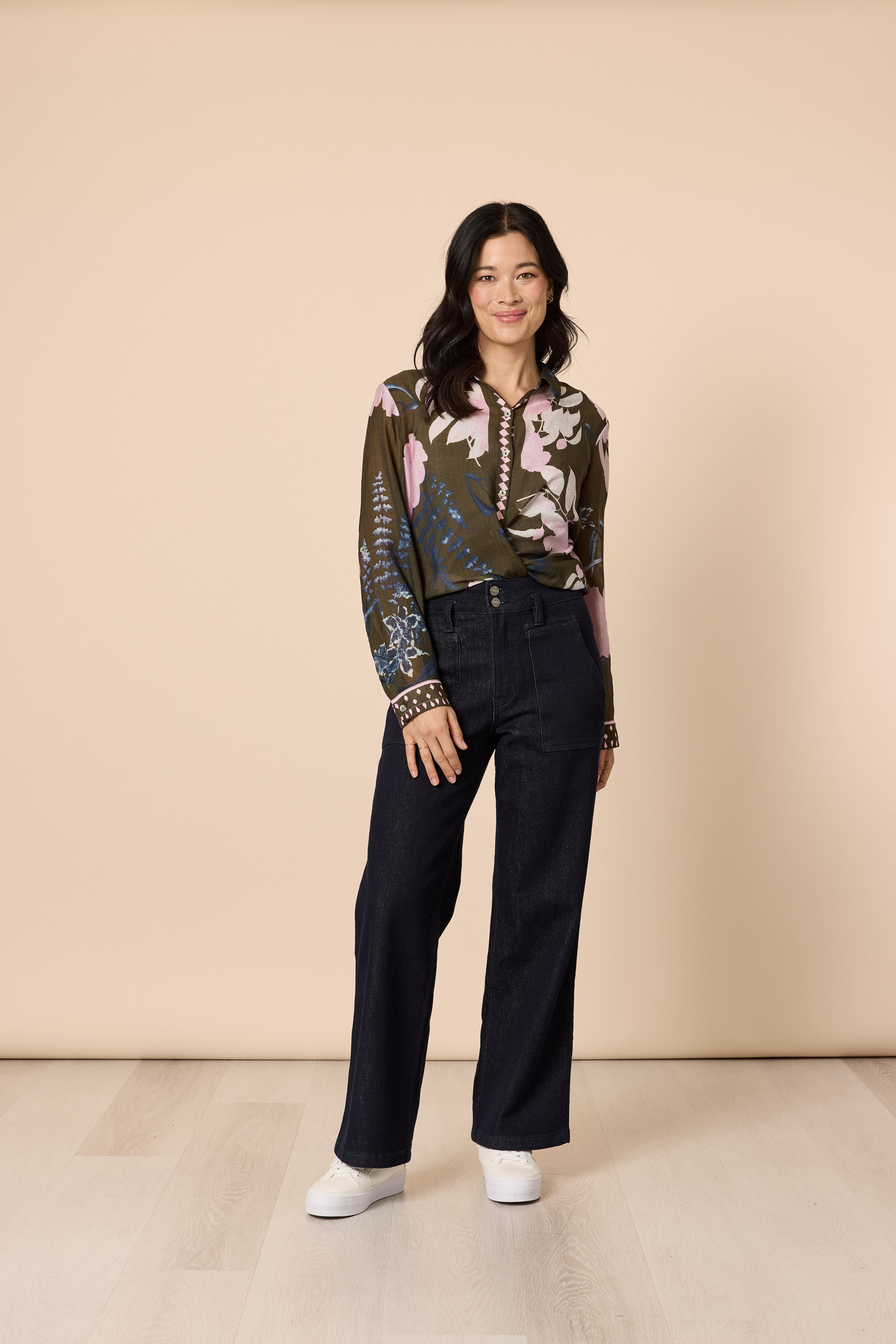 Side pose woman in printed khaki blouse with dark denim casual jeans