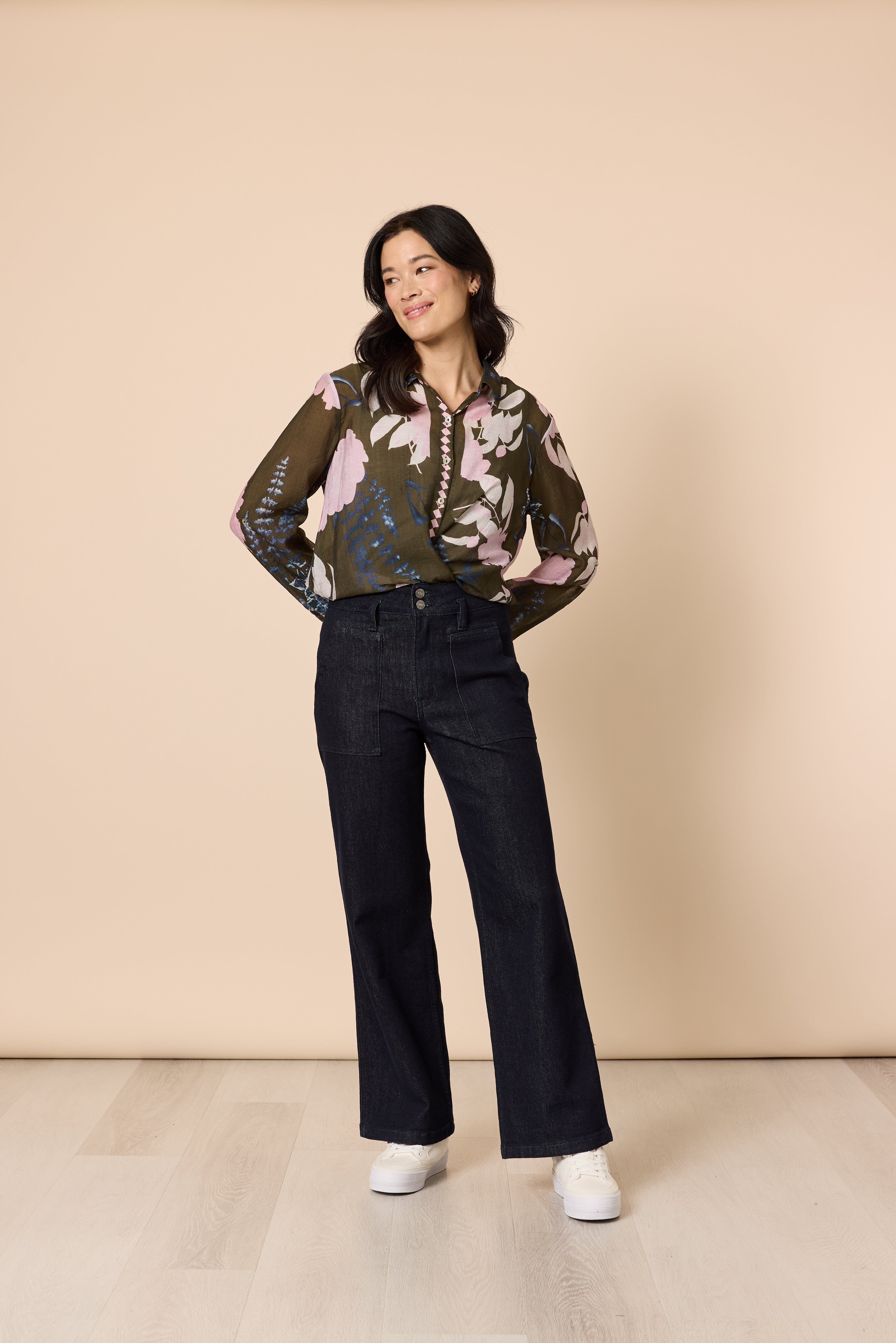 Fashion model in floral blouse and dark denim jeans minimal studio background