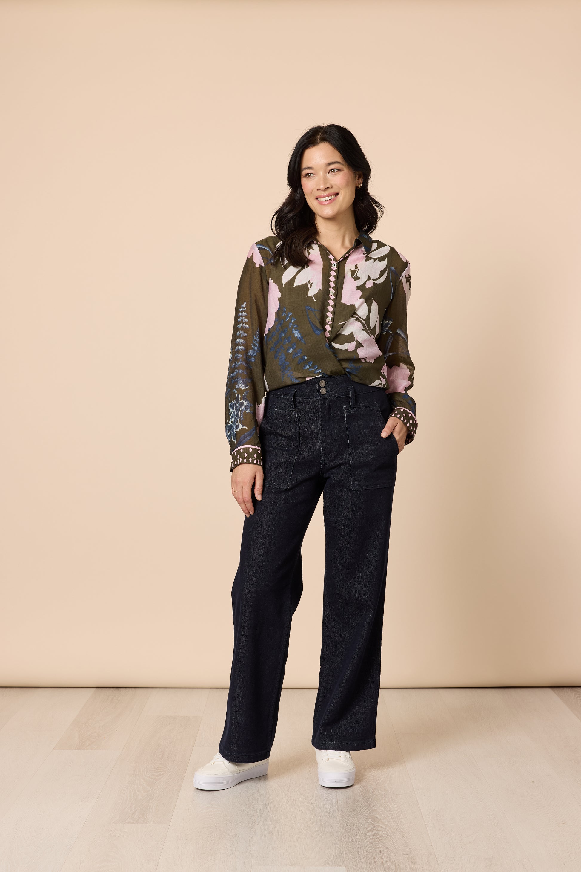 Smiling model in floral patterned blouse and dark wash denim relaxed stance