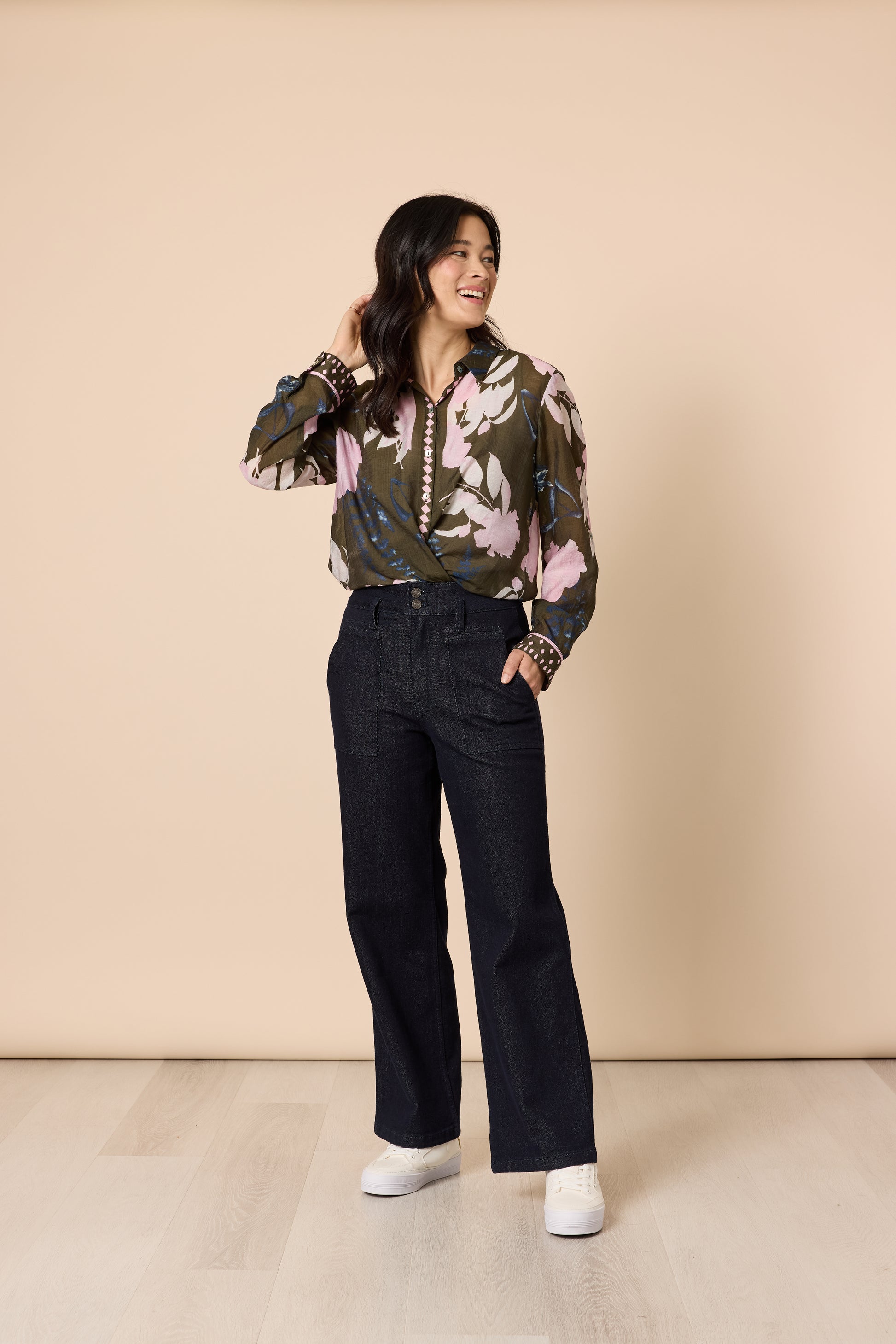 Stylish woman posing in floral shirt and dark denim wide leg trousers