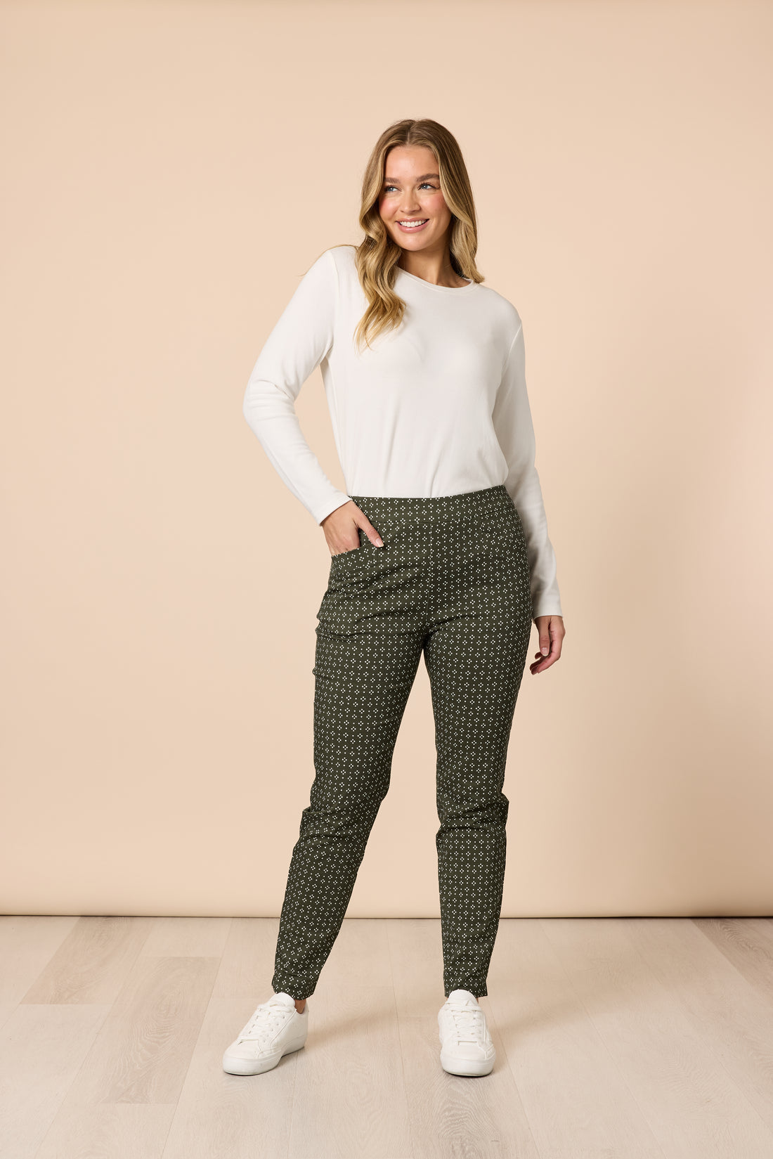 Woman wearing a classic ivory long sleeve basic top with olive printed pants and white sneakers, full body casual outfit on a beige background Showies Boutique