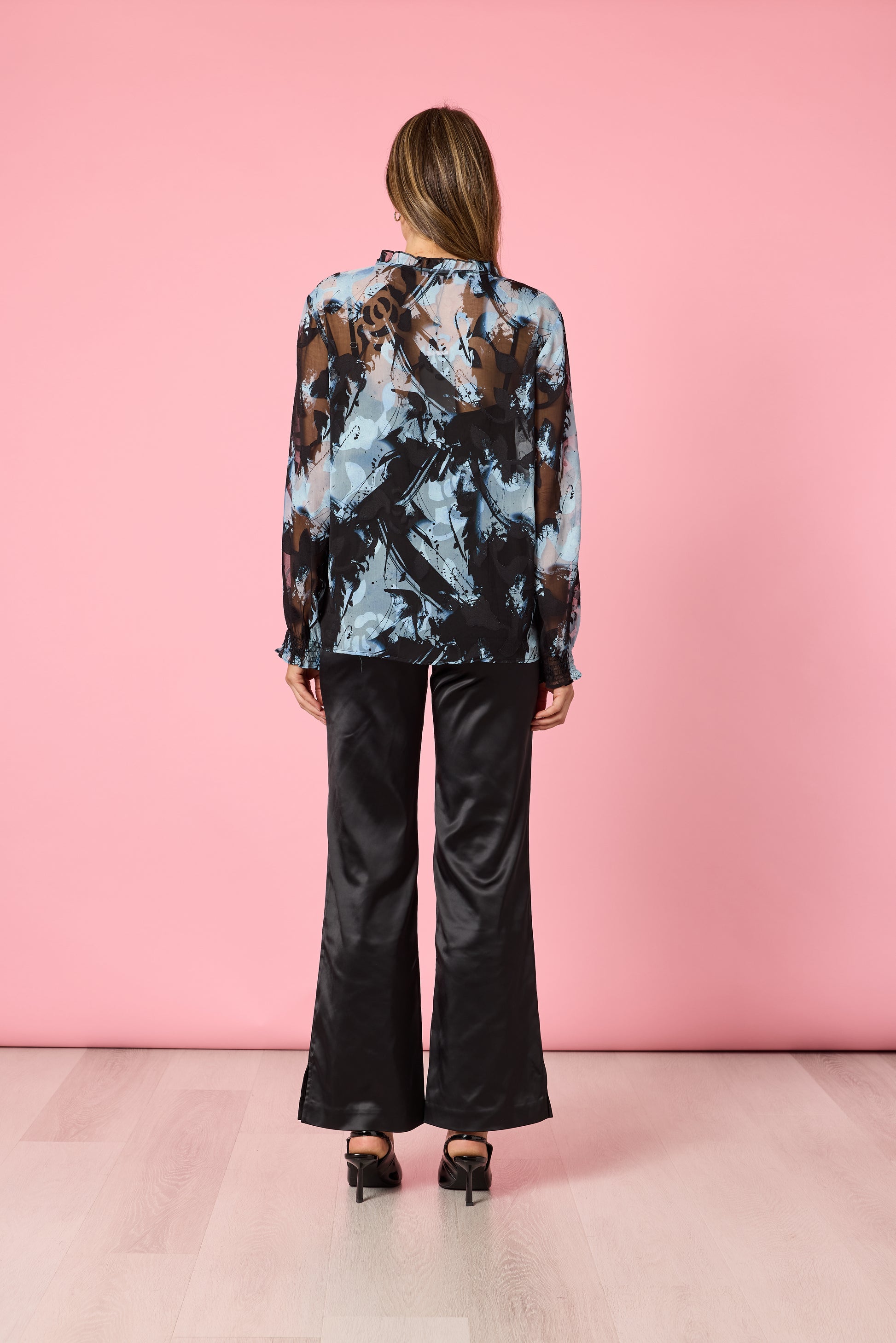 Back view of woman in blue patterned blouse and black pants on pink background