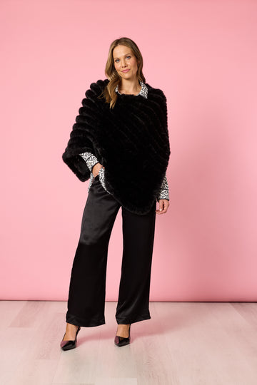 Woman in black faux fur poncho with wide leg pants on pink background