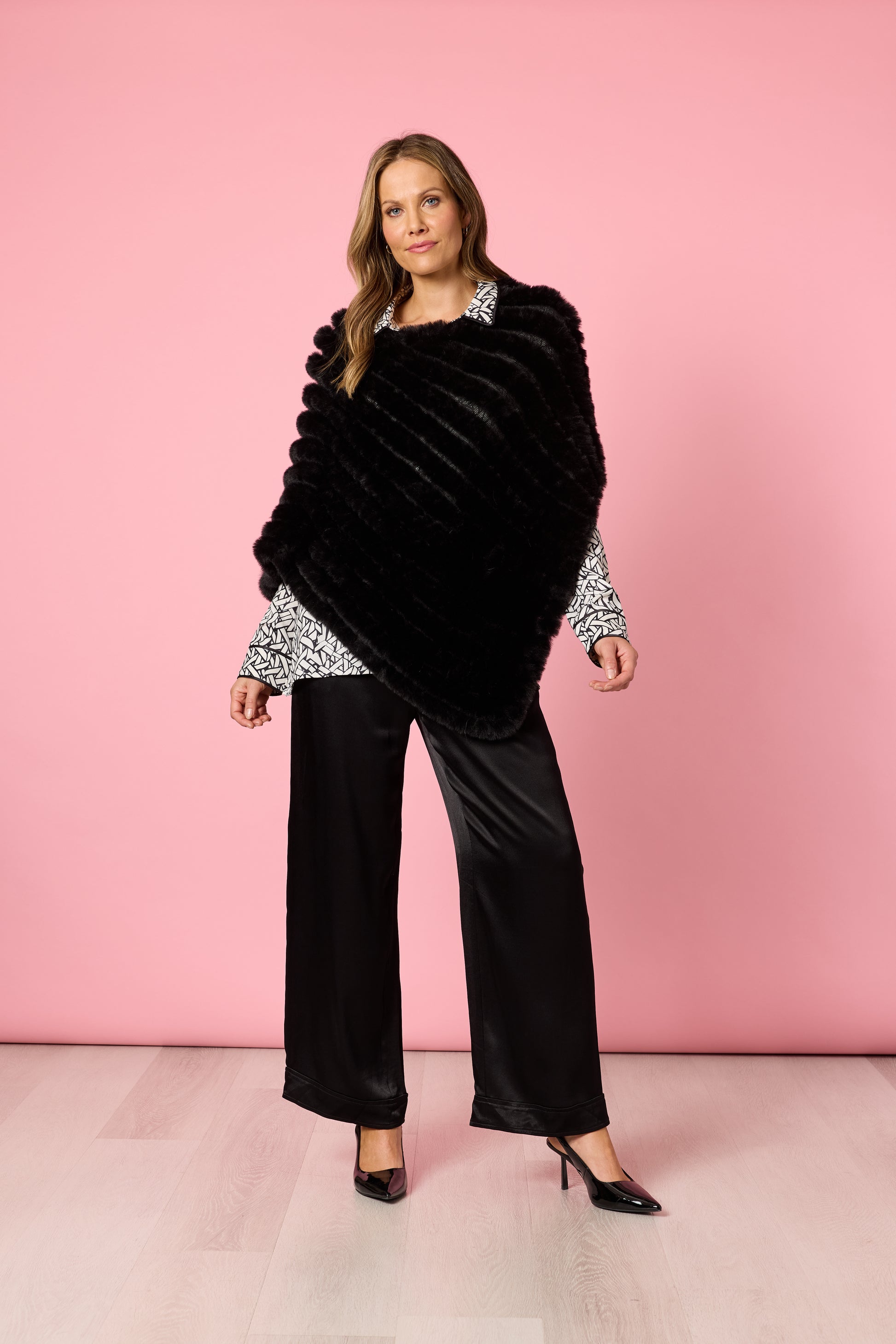 Woman posing in black poncho layered over patterned blouse and black trousers