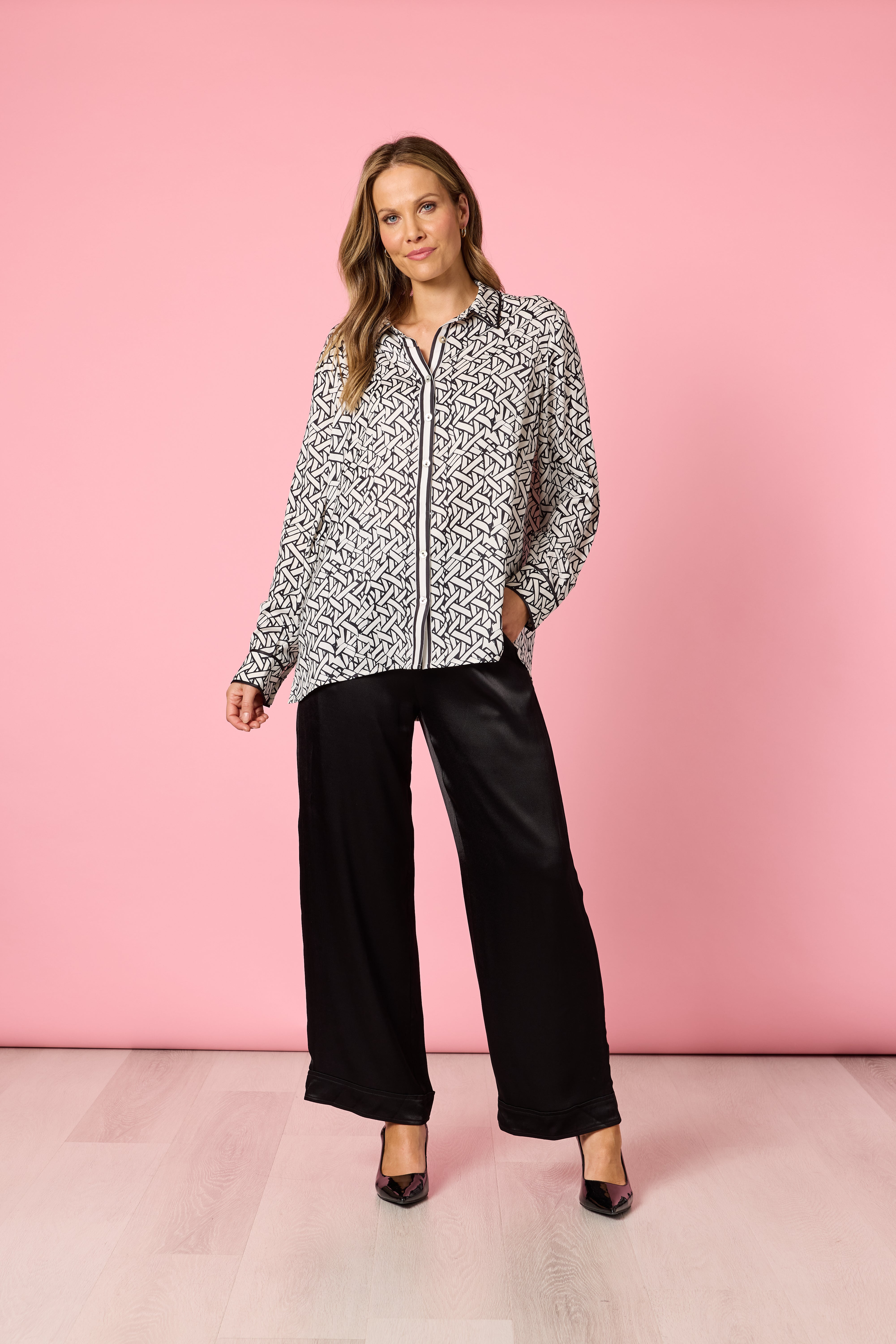 Fashion model in monochrome printed blouse and black pants posing on pink backdrop