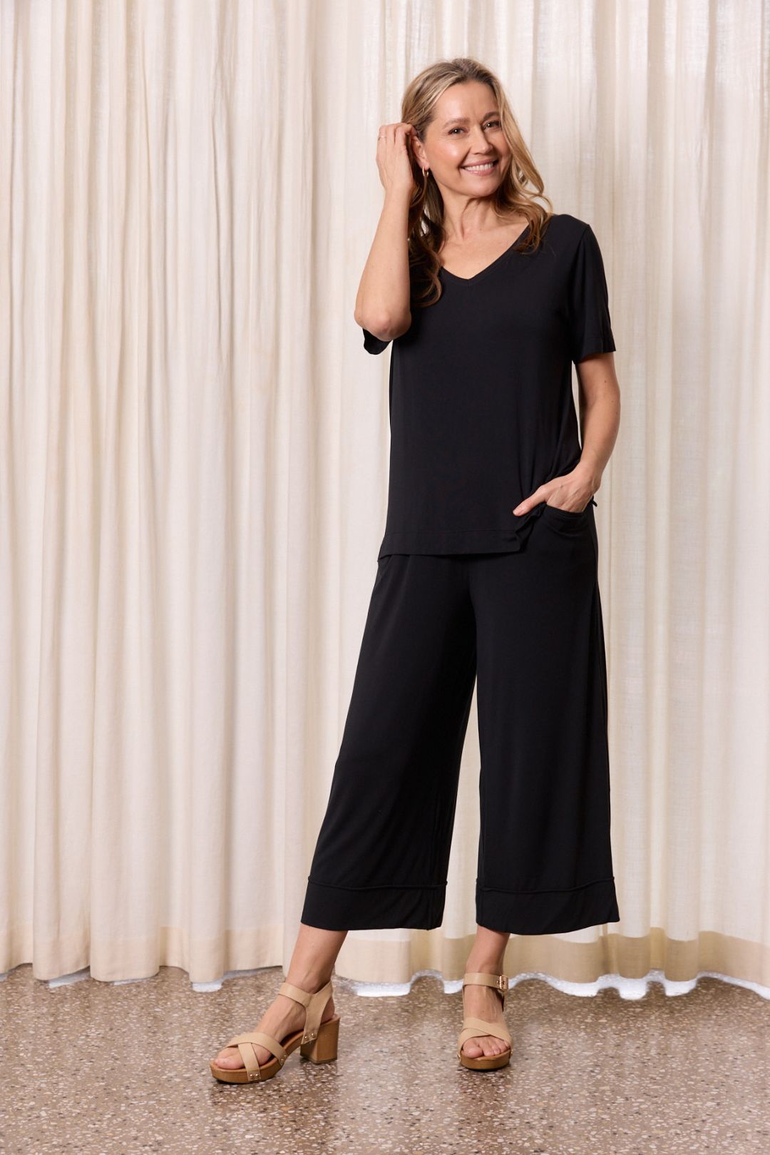 Woman in black lounge outfit smiling relaxed indoor fashion look