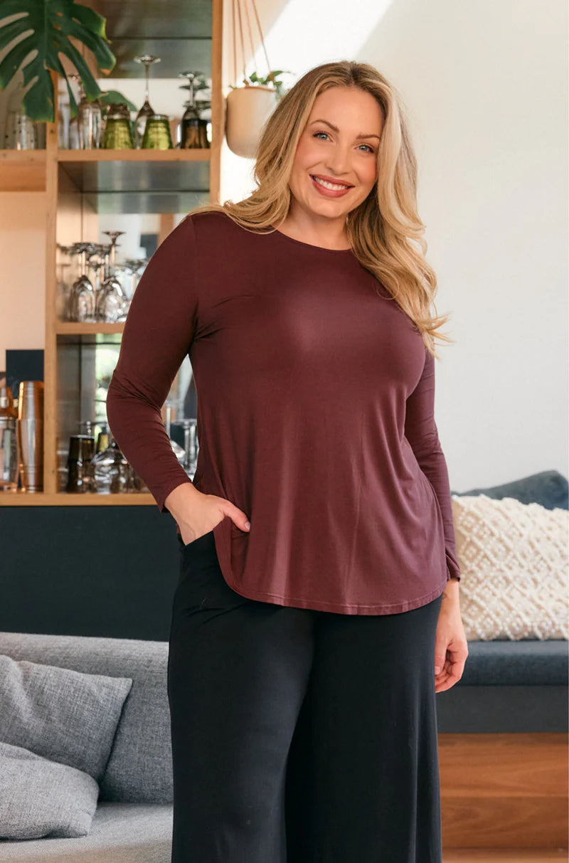 Woman wearing a merlot long sleeve tunic top with black wide leg pants, front view relaxed fit outfit in a modern living room, casual everyday styling Showies Boutique