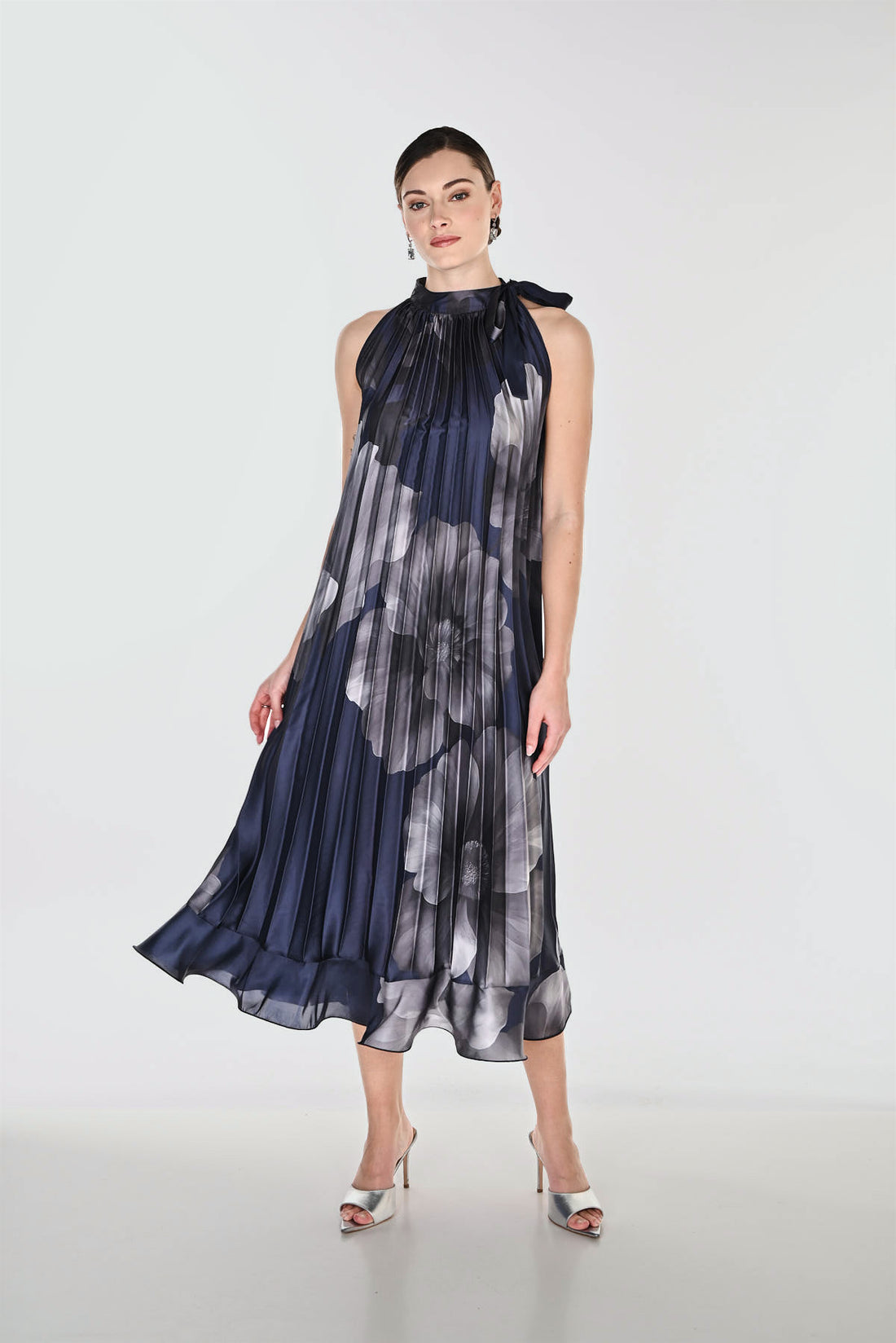 Navy blue and grey pleated midi dress featuring a floral print, high neckline with tie detail, and flowing A-line silhouette for elegant occasion wear.
