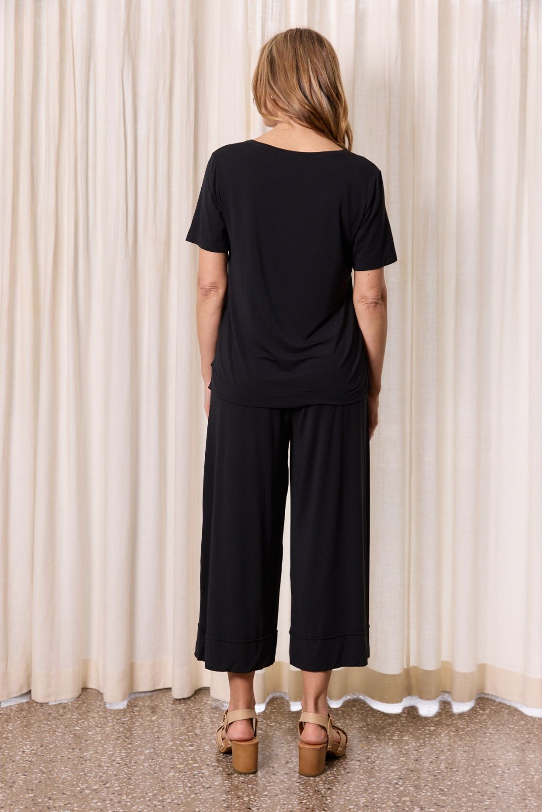 Back view of black casual outfit with wide leg pants against curtain