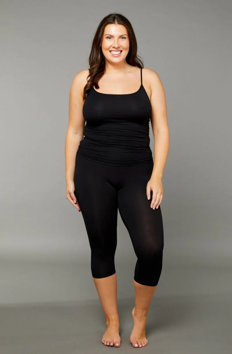 Woman wearing a black scoop neck tank top with black 7/8 capri leggings on grey background