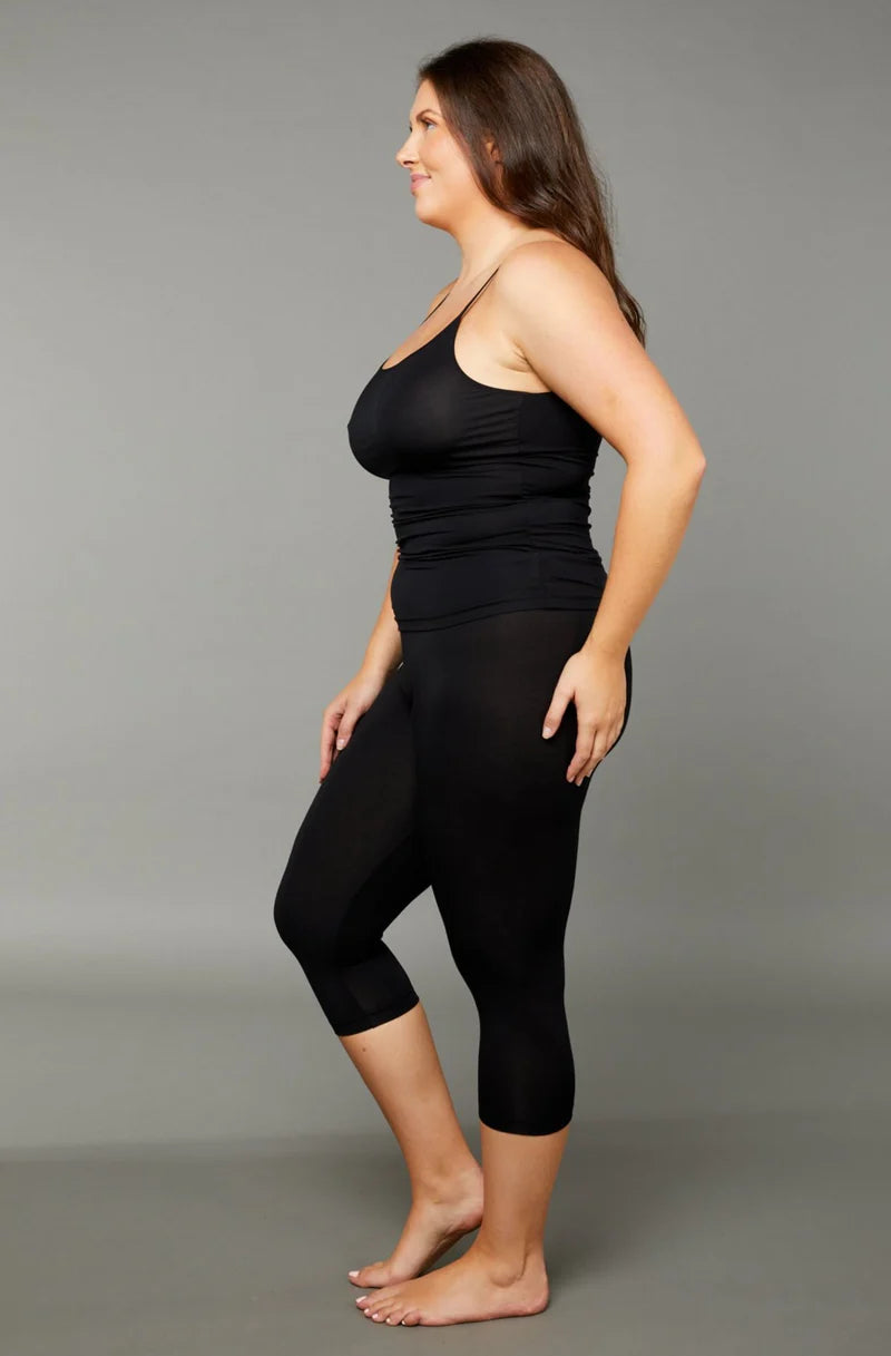 Woman wearing a black scoop neck tank top with black 7/8 capri leggings side view on grey background