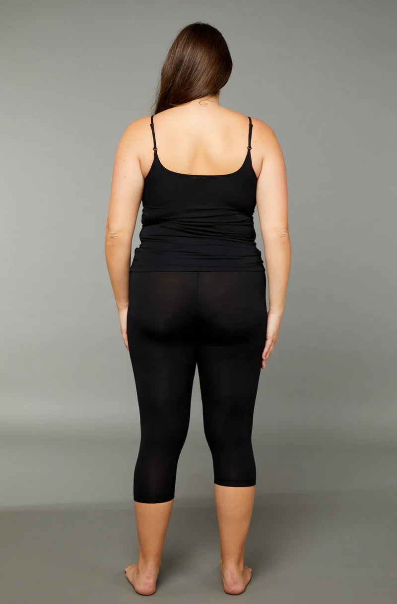 Woman wearing a black scoop neck tank top with black 7/8 capri leggings back view on grey background