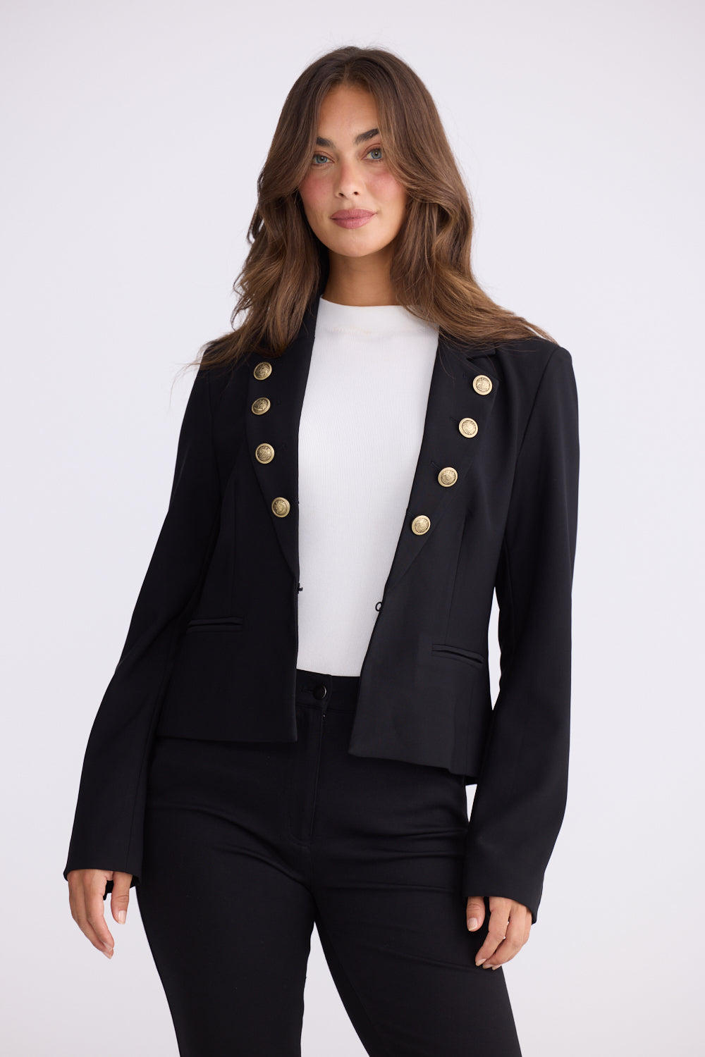 Woman wearing black tailored blazer with gold buttons, white top, black pants and boots
