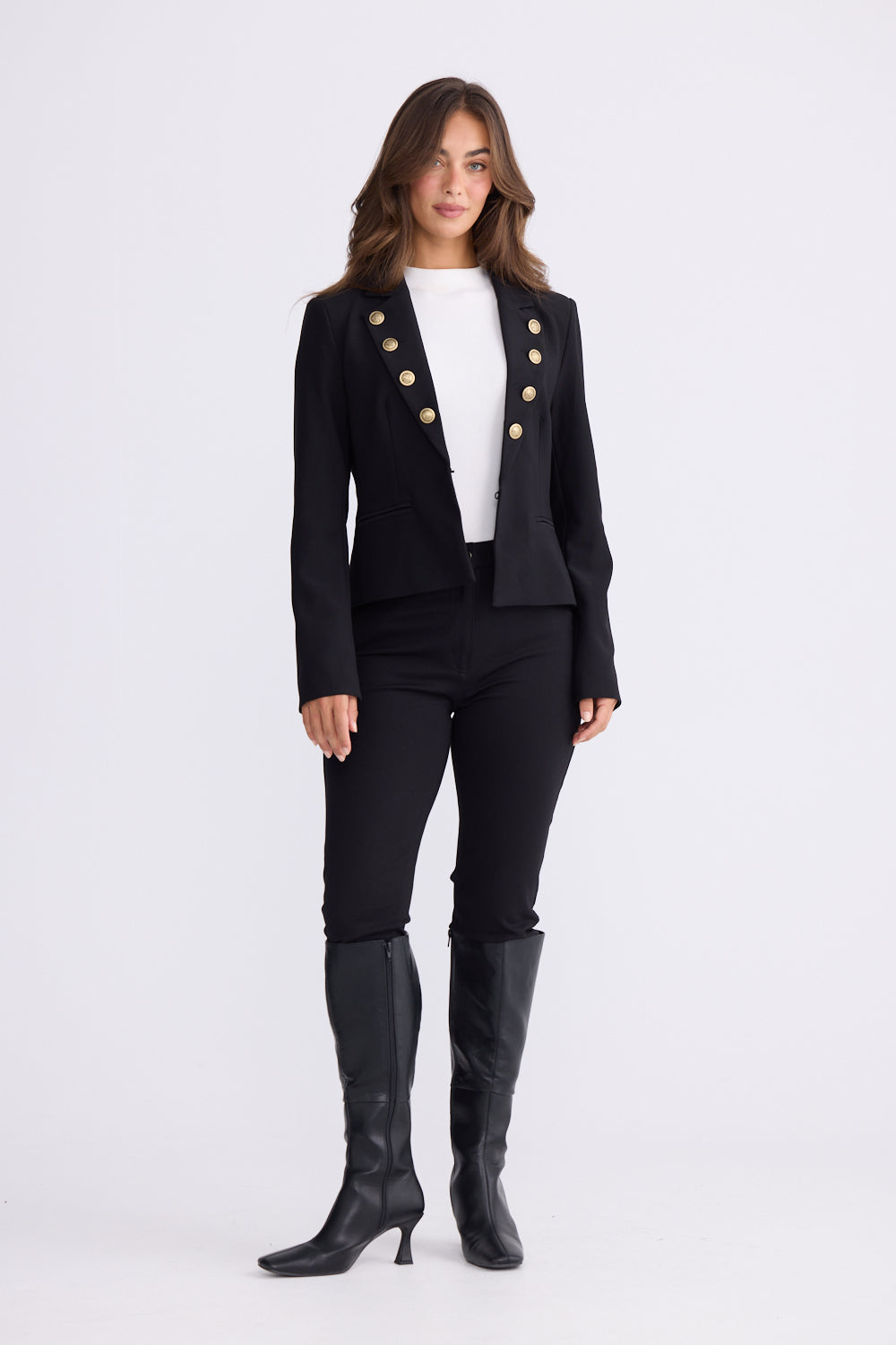 Woman in black fitted blazer styled with white top, black pants and knee-high boots