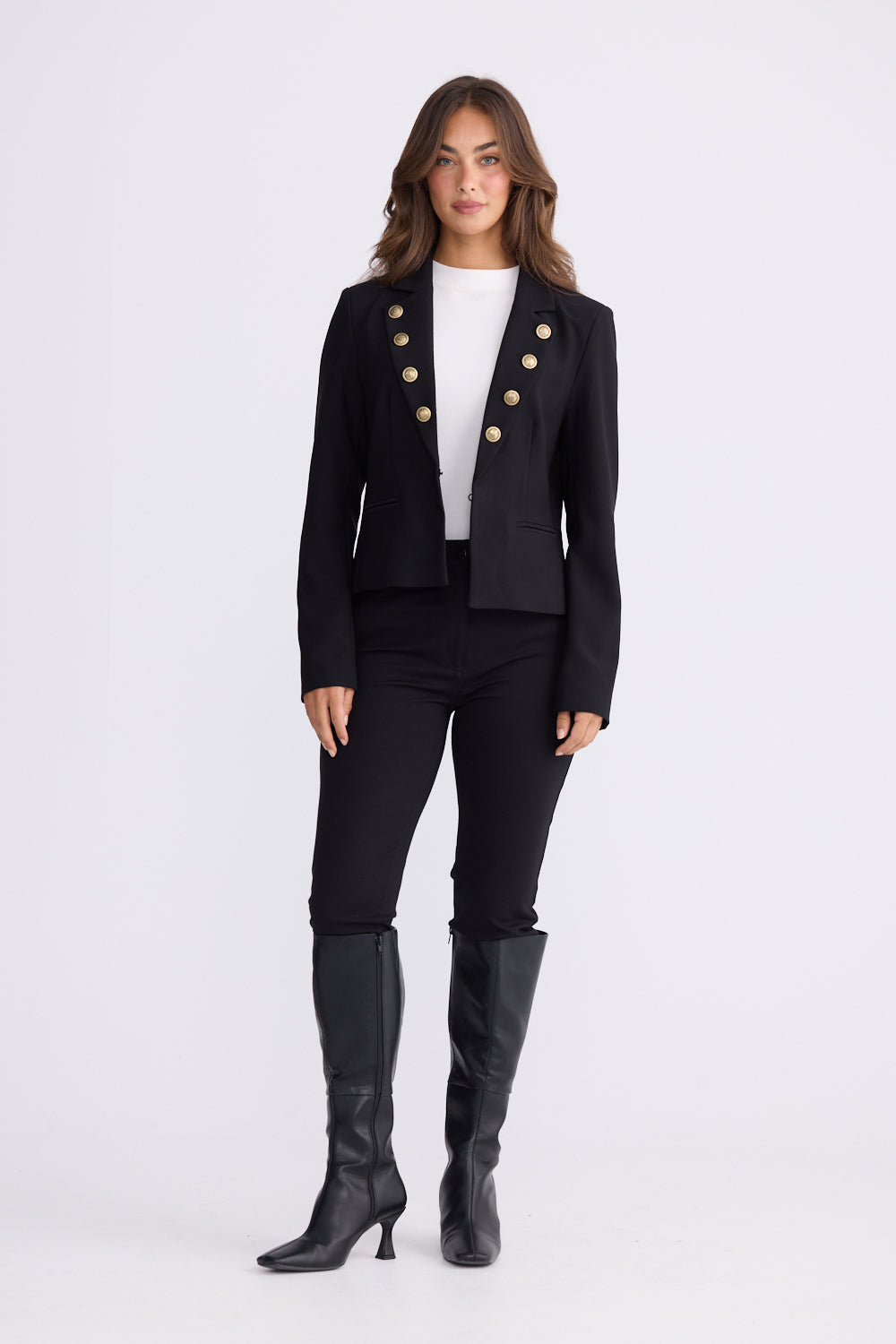 Woman wearing black tailored blazer with gold buttons, white top, black pants and boots