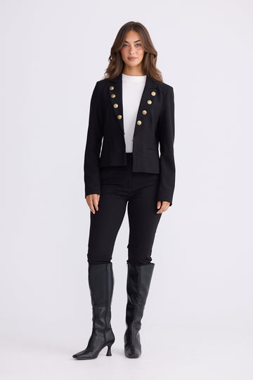 Woman wearing black tailored blazer with gold buttons, white top, black pants and boots