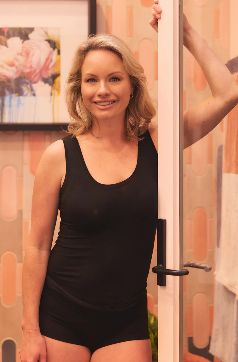 Woman wearing a black scoop neck bodysuit standing indoors with modern wall art background