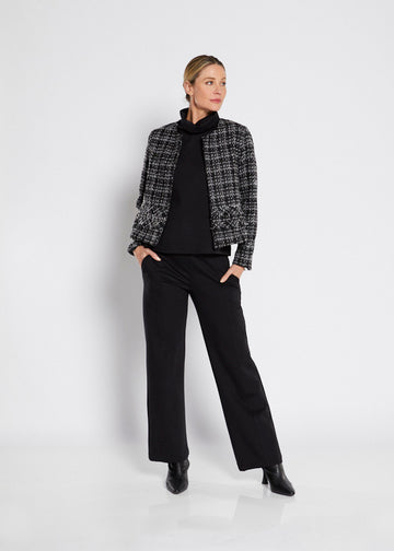 Woman wearing a black and white checkered jacket over a black turtleneck and pants on a white background.