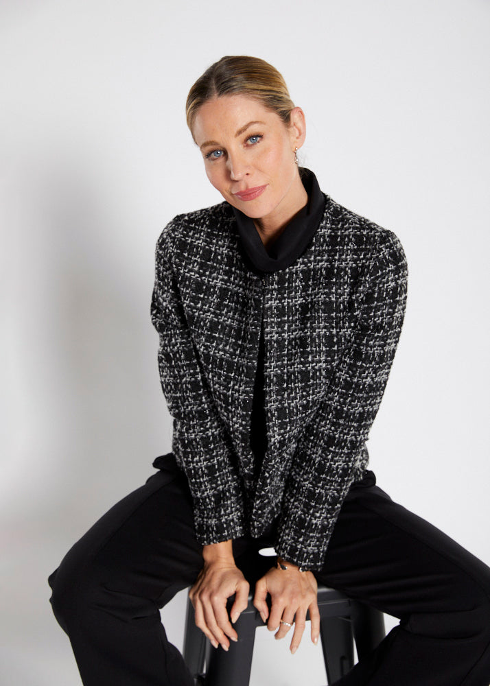 A woman wearing a black and white patterned jacket is sitting down on a white background.