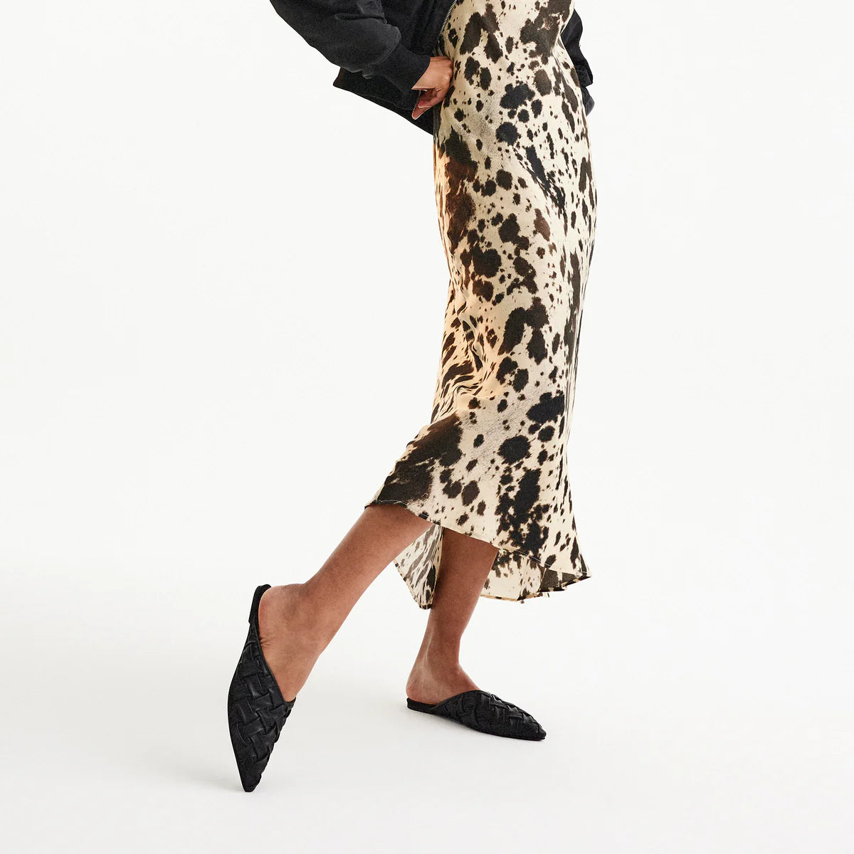 Woman wearing black woven pointed mule sandals with printed skirt
