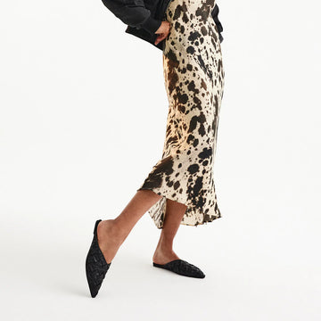 Woman wearing black woven pointed mule sandals with printed skirt