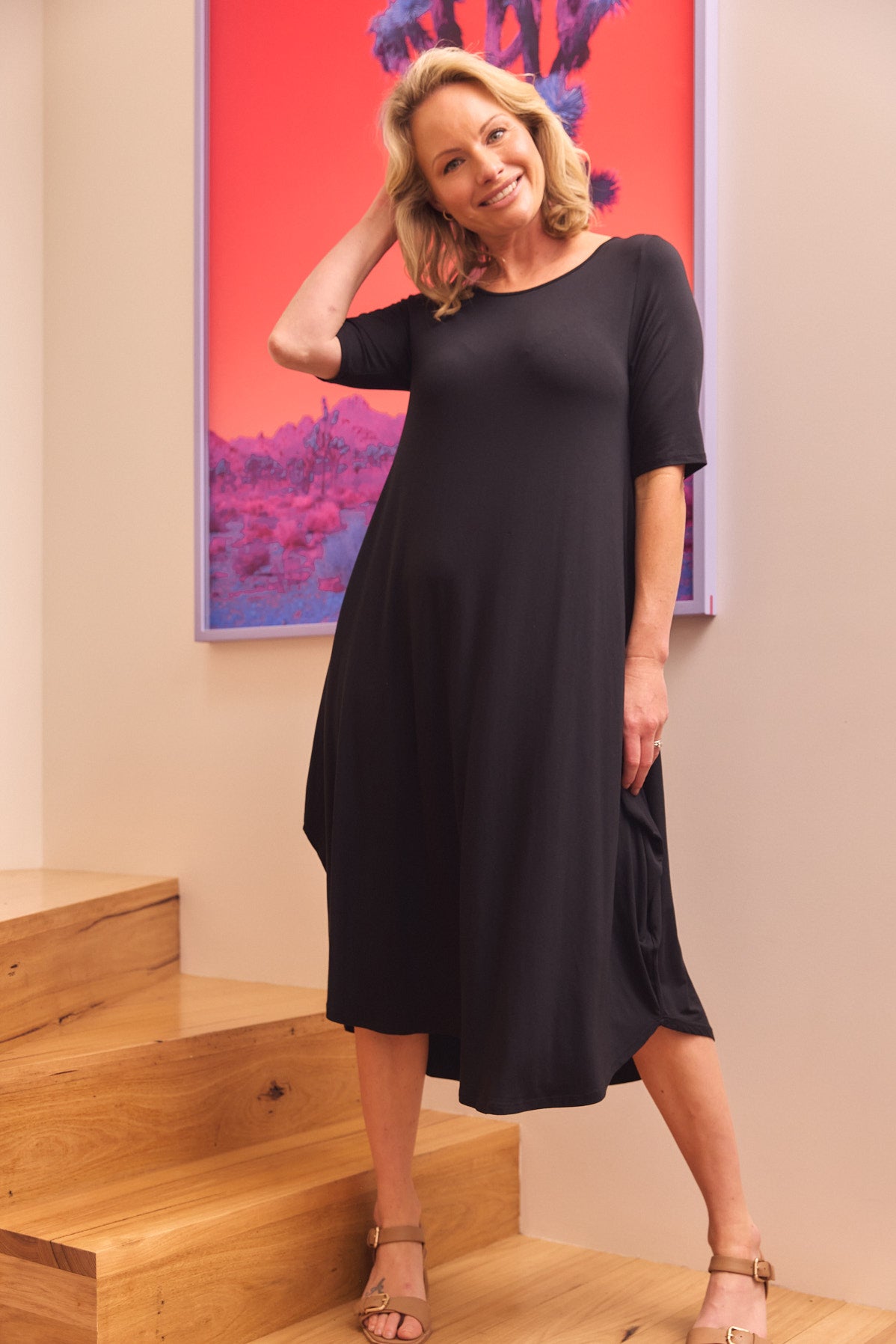 Woman in black loose fit dress posing on wooden stairs modern casual style