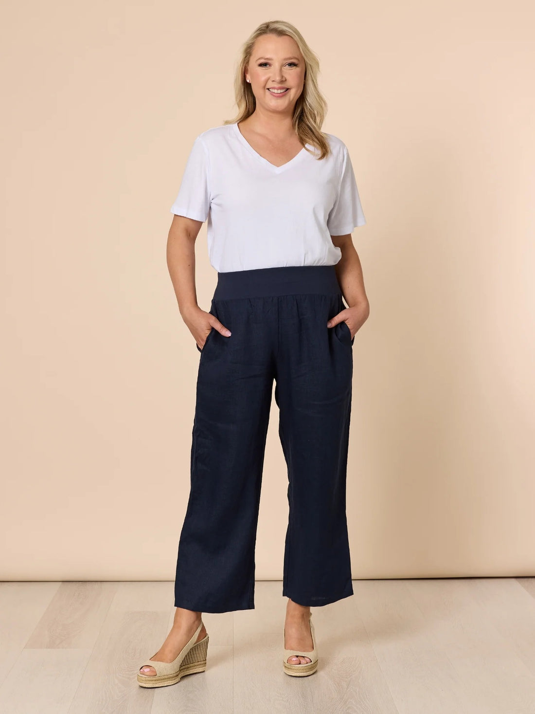 Women’s navy wide leg denim pants with elastic waistband and pockets, styled with white top and wedge sandals, front view from Showies Boutique Adelaide