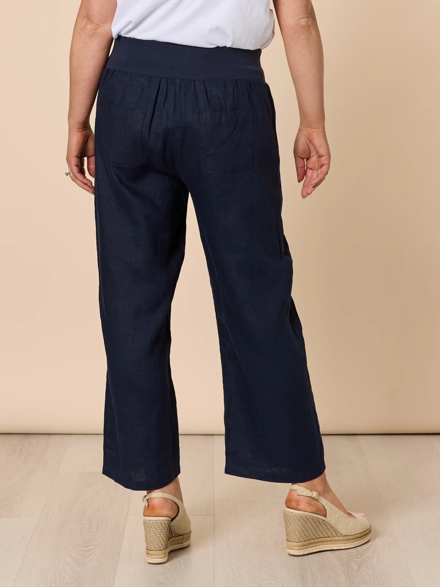 Back view of navy wide leg denim pants with elastic waistband and relaxed fit, styled with white top and wedge sandals, from Showies Boutique Adelaide