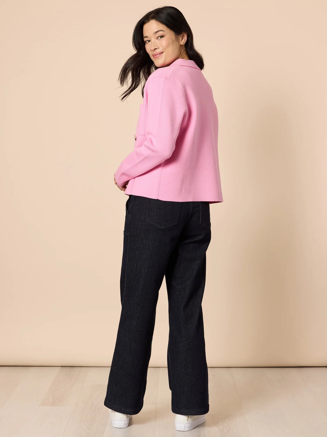 Back angled view of woman wearing pink knit collar cardigan with structured silhouette and button front, paired with dark denim pants, from Showies Boutique Adelaide
