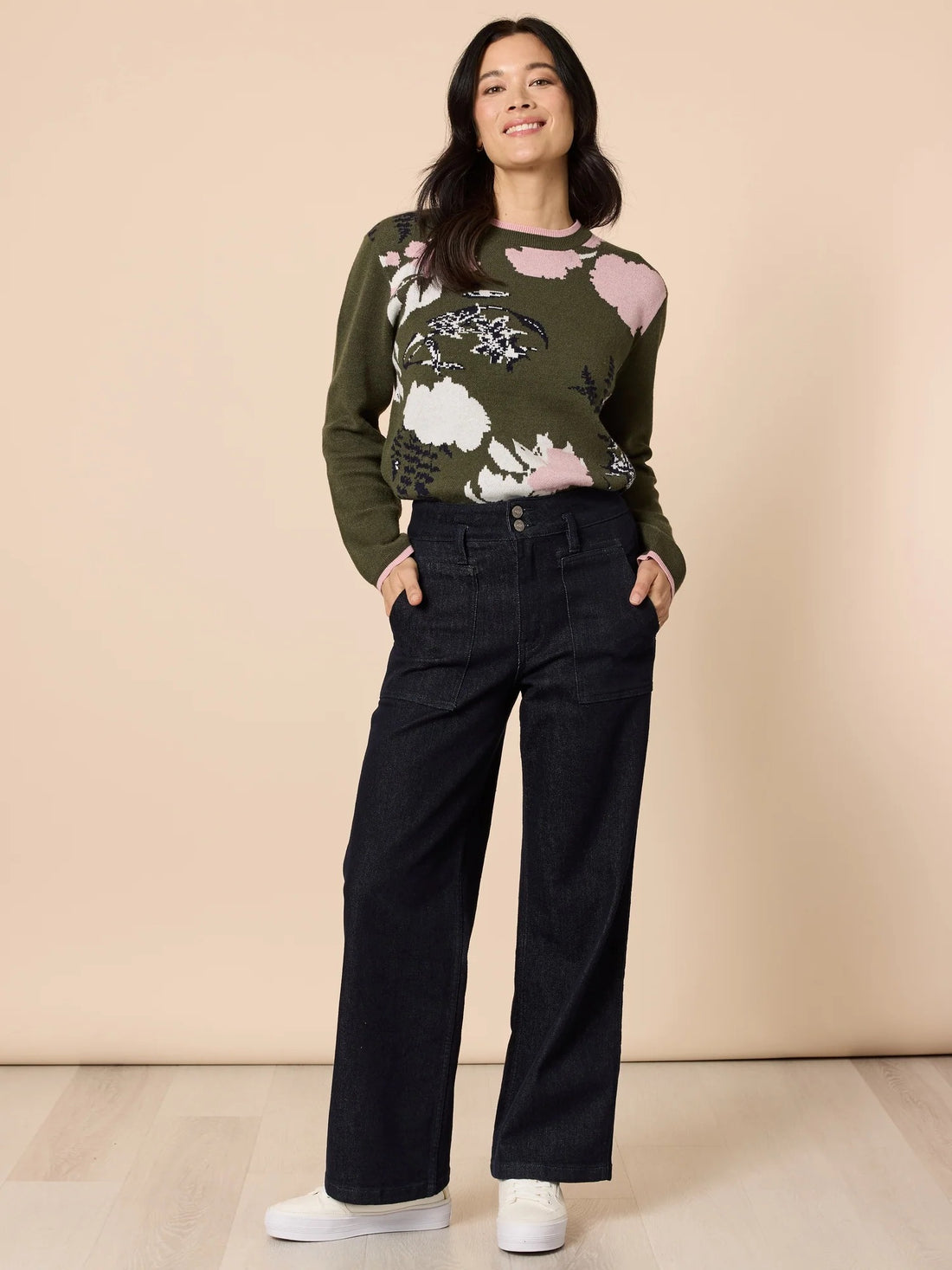 Woman wearing a khaki floral knit jumper paired with dark wide-leg denim jeans and white sneakers against a beige background