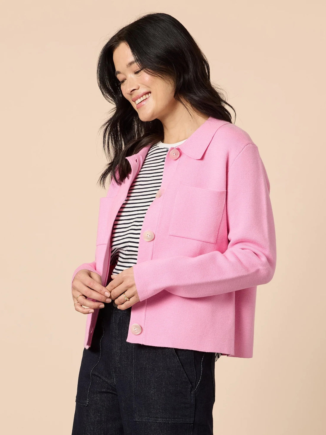 Back angled view of woman wearing pink knit collar cardigan with structured silhouette and button front, paired with dark denim pants, from Showies Boutique Adelaide