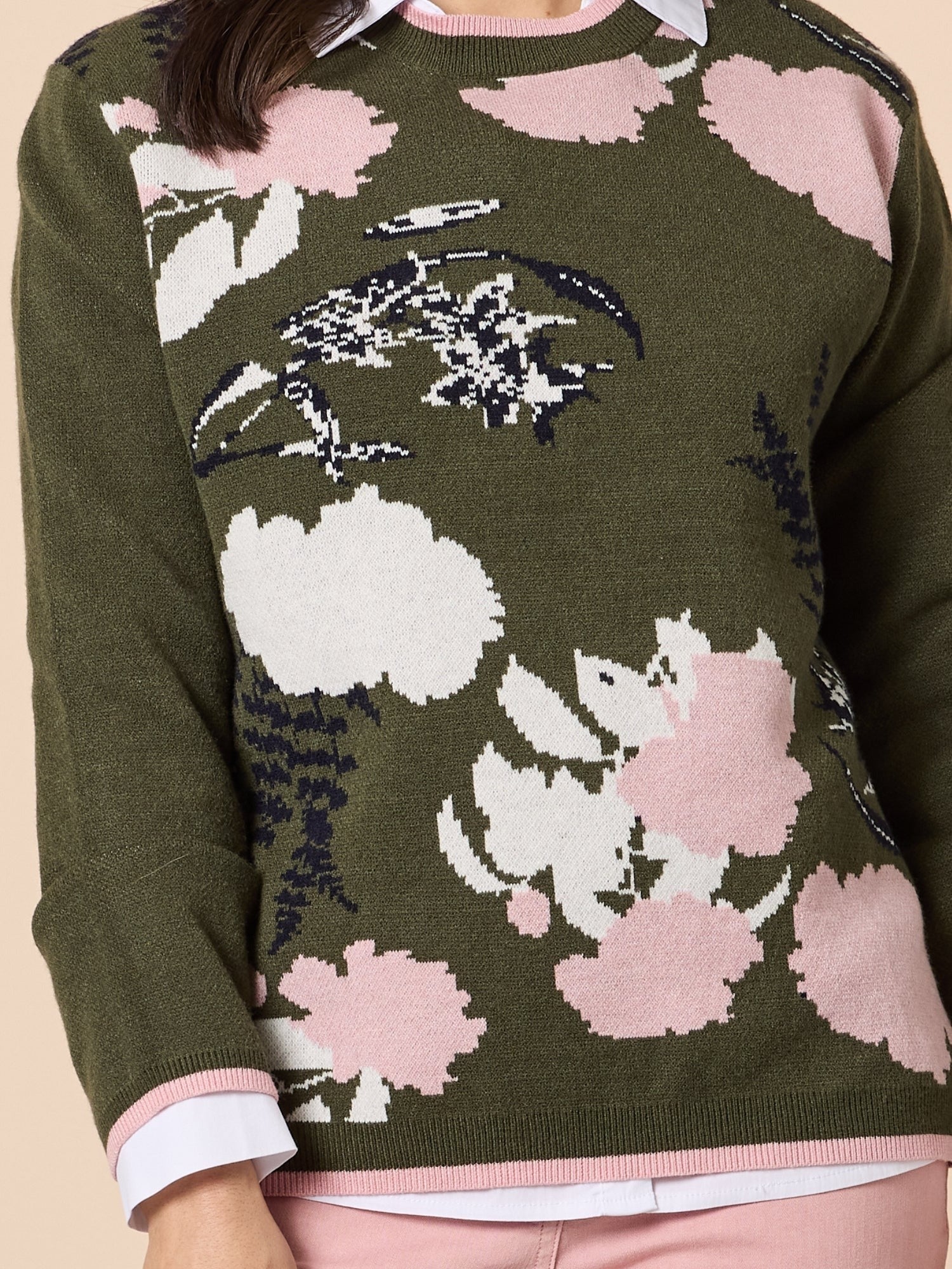 Close-up of a khaki green knit sweater featuring soft pink and white floral patterns, worn over a collared shirt, highlighting the texture and design details