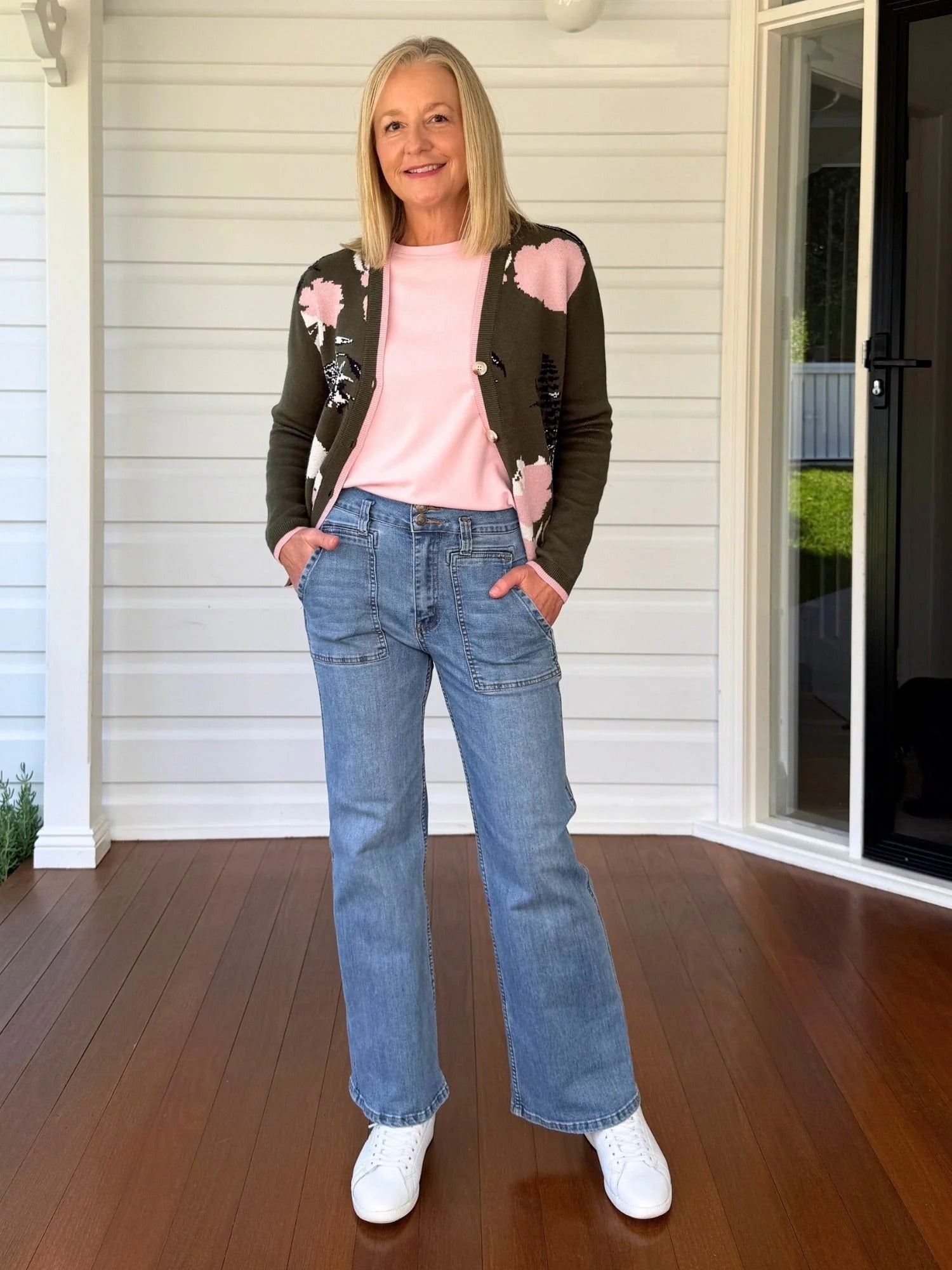 Woman wearing khaki floral knit cardigan with pink trim, styled with blush top and blue denim jeans, casual outfit look from Showies Boutique Adelaide