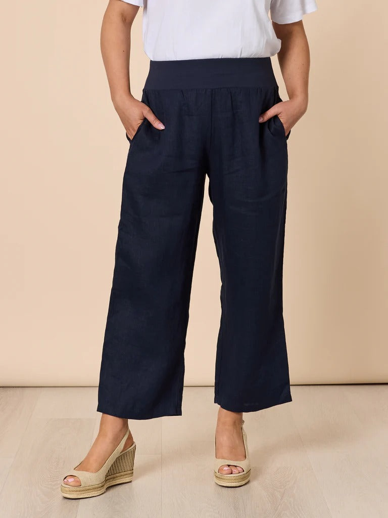 Women’s navy wide leg denim pants with elastic waistband and pockets, styled with white top and wedge sandals, front view from Showies Boutique Adelaide