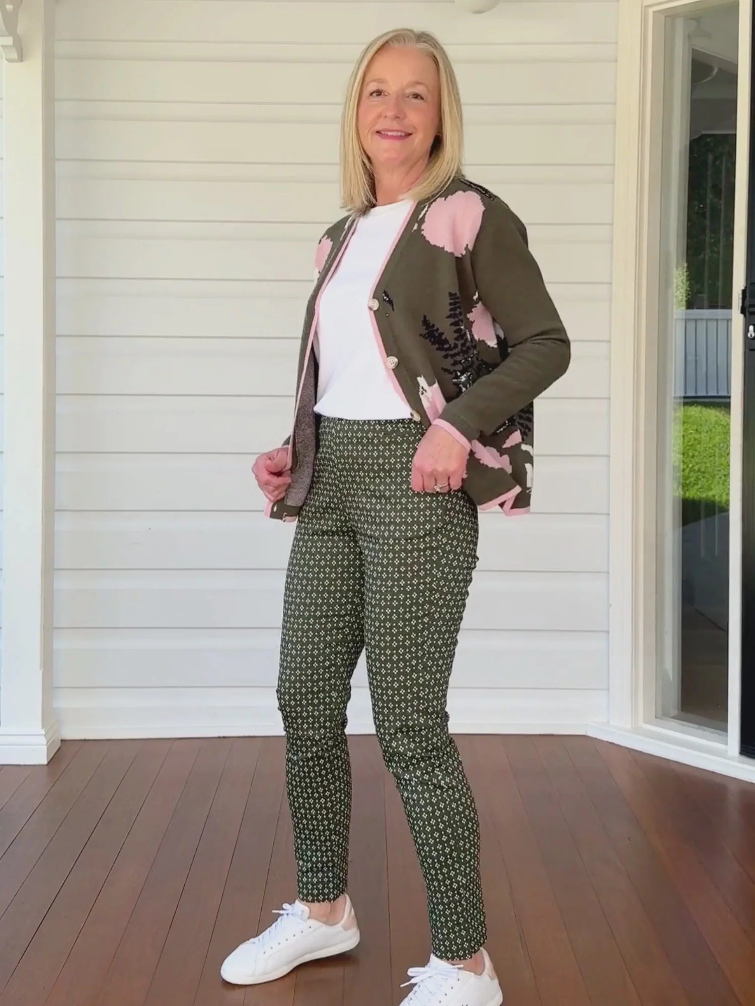 Woman styling khaki floral knit cardigan with pink trim, paired with printed green pants and white top, casual outfit look from Showies Boutique Adelaide
