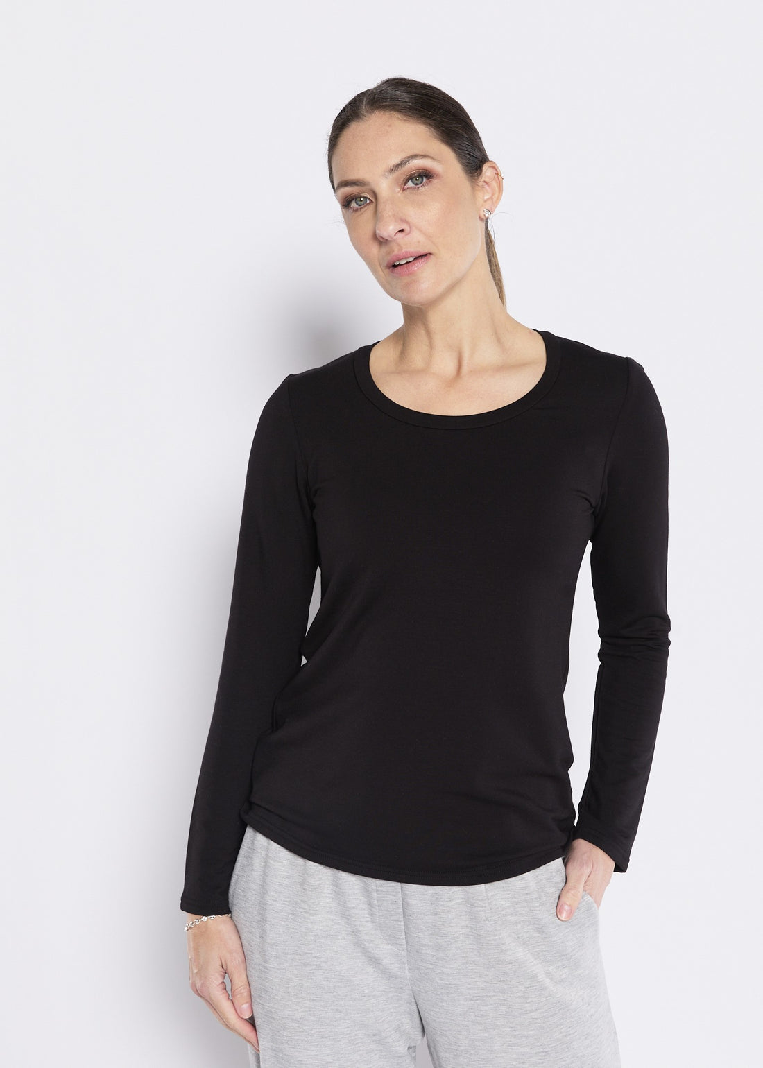Woman wearing a black long sleeve crew neck top with grey lounge pants on a light background