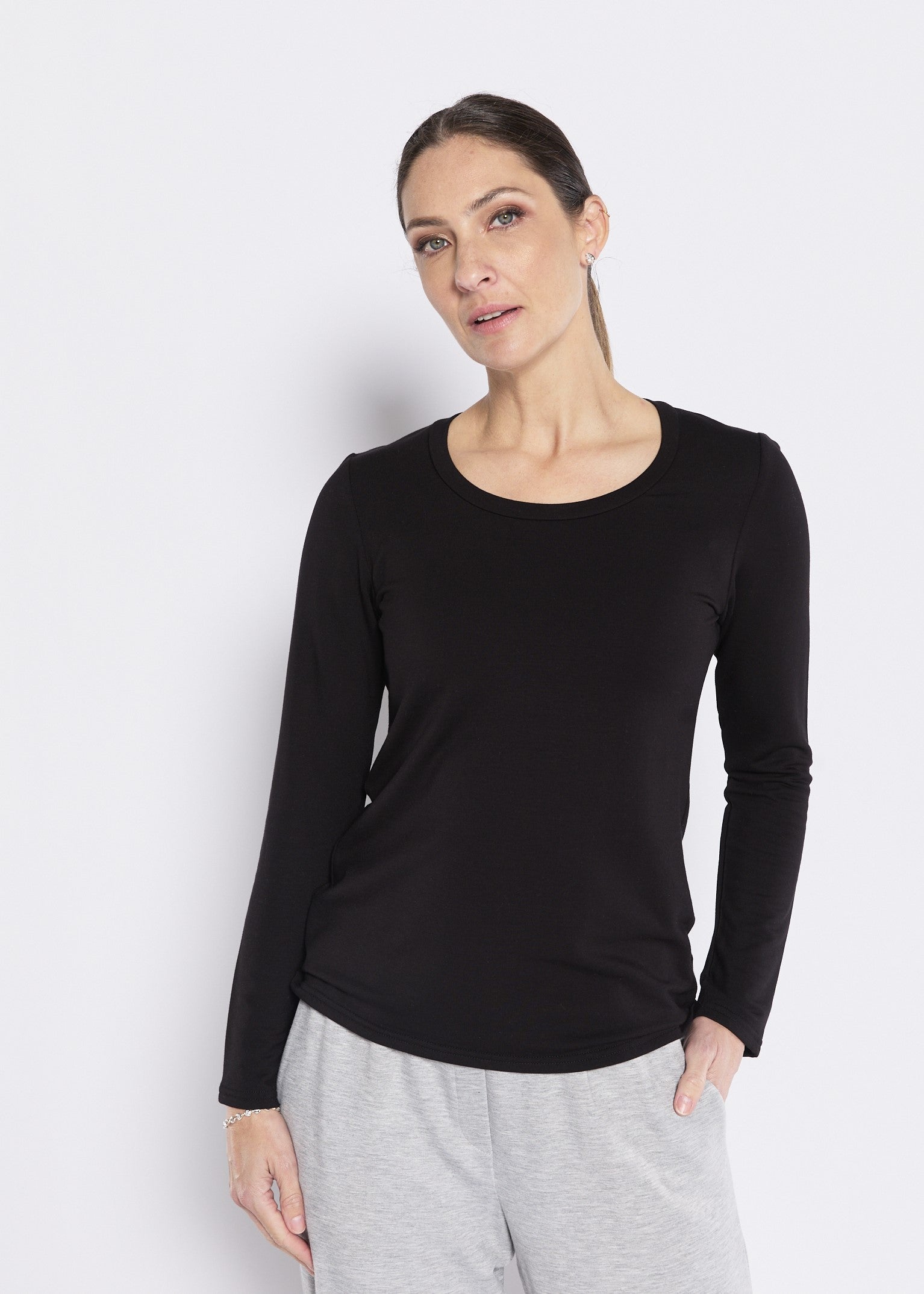 Woman wearing a black long sleeve crew neck top with grey lounge pants on a light background