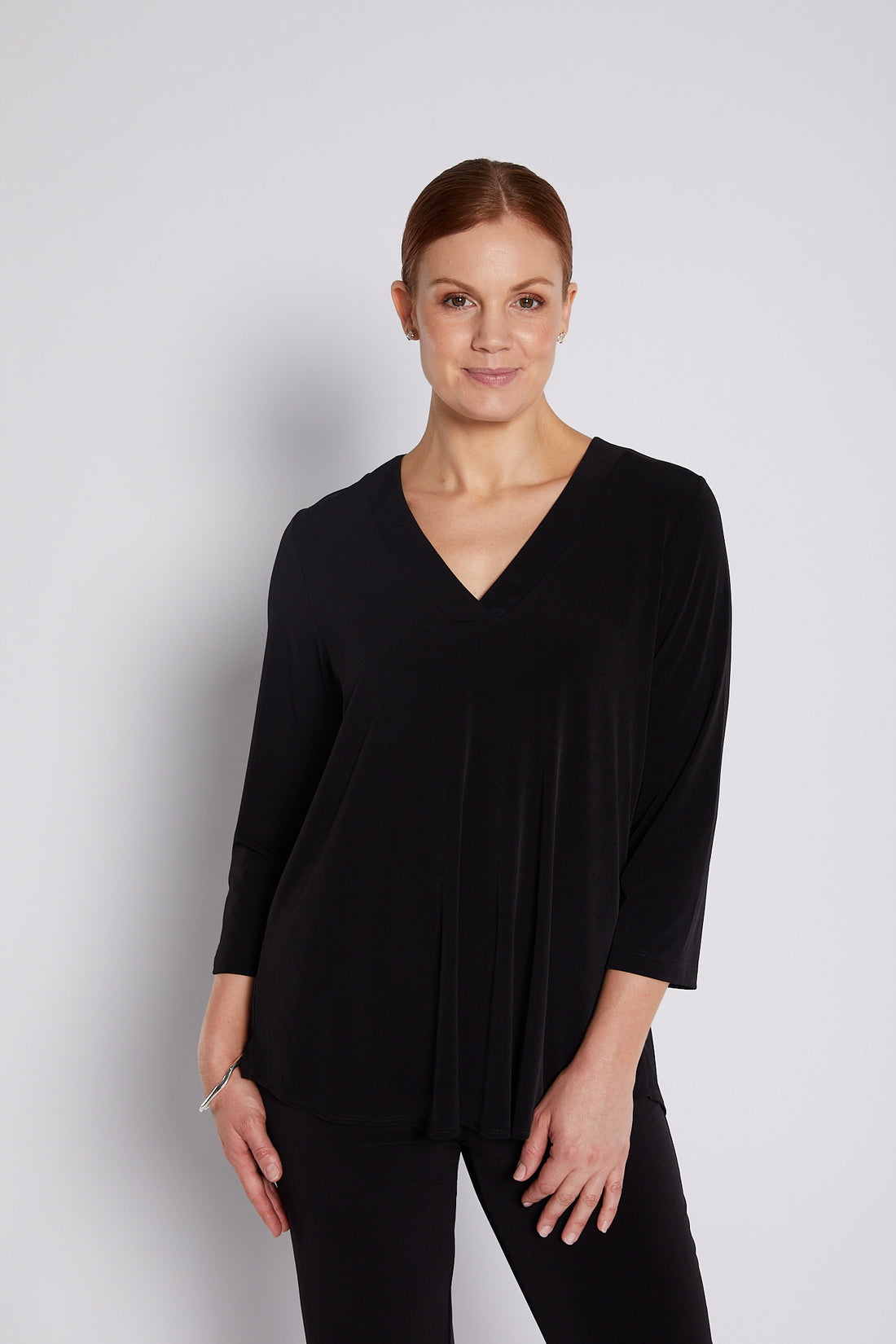 Woman wearing a black V-neck swing top and black pants on a light background