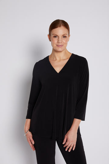 Woman wearing a black V-neck swing top and black pants on a light background