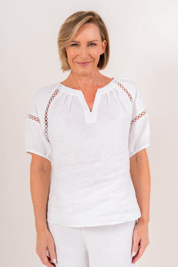 White linen embroidered top featuring a V-neckline, delicate cutwork detailing, short sleeves, and a relaxed silhouette for elegant everyday styling.